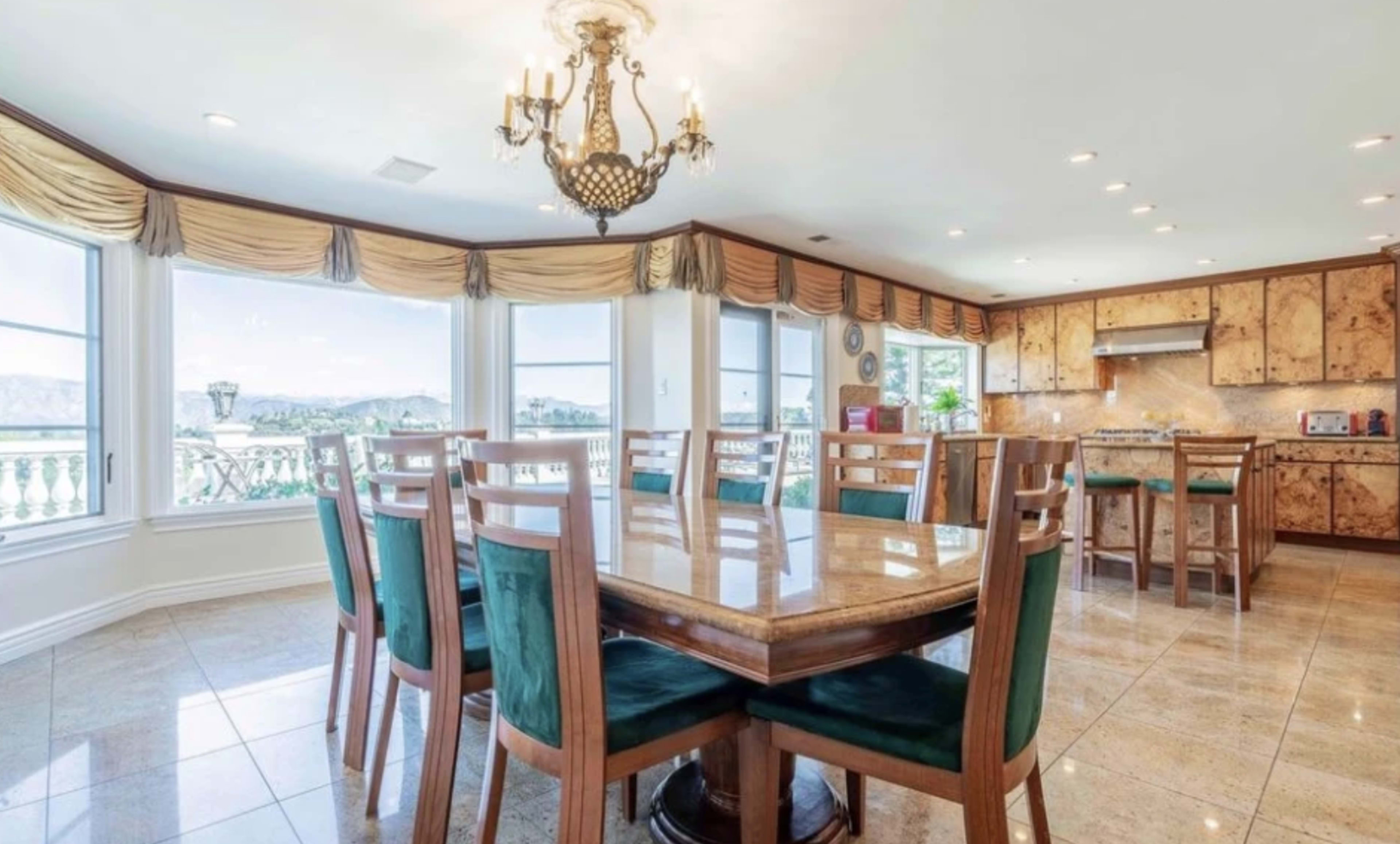 A spacious dining area features a large table surrounded by green upholstered chairs, with windows providing a view of the outdoors.