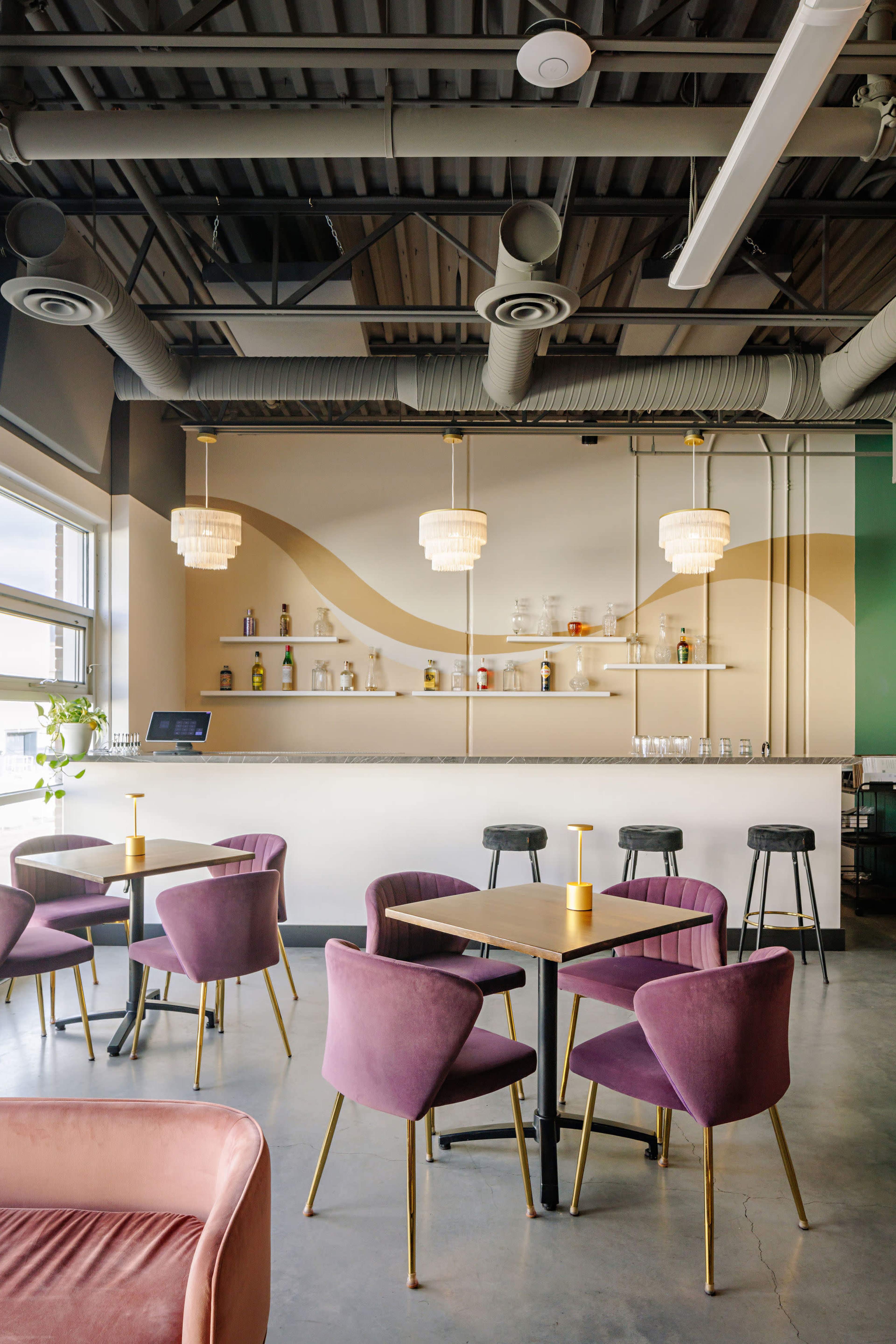 A modern café features a bar with shelves displaying bottles, surrounded by elegant seating in purple and gold tones.