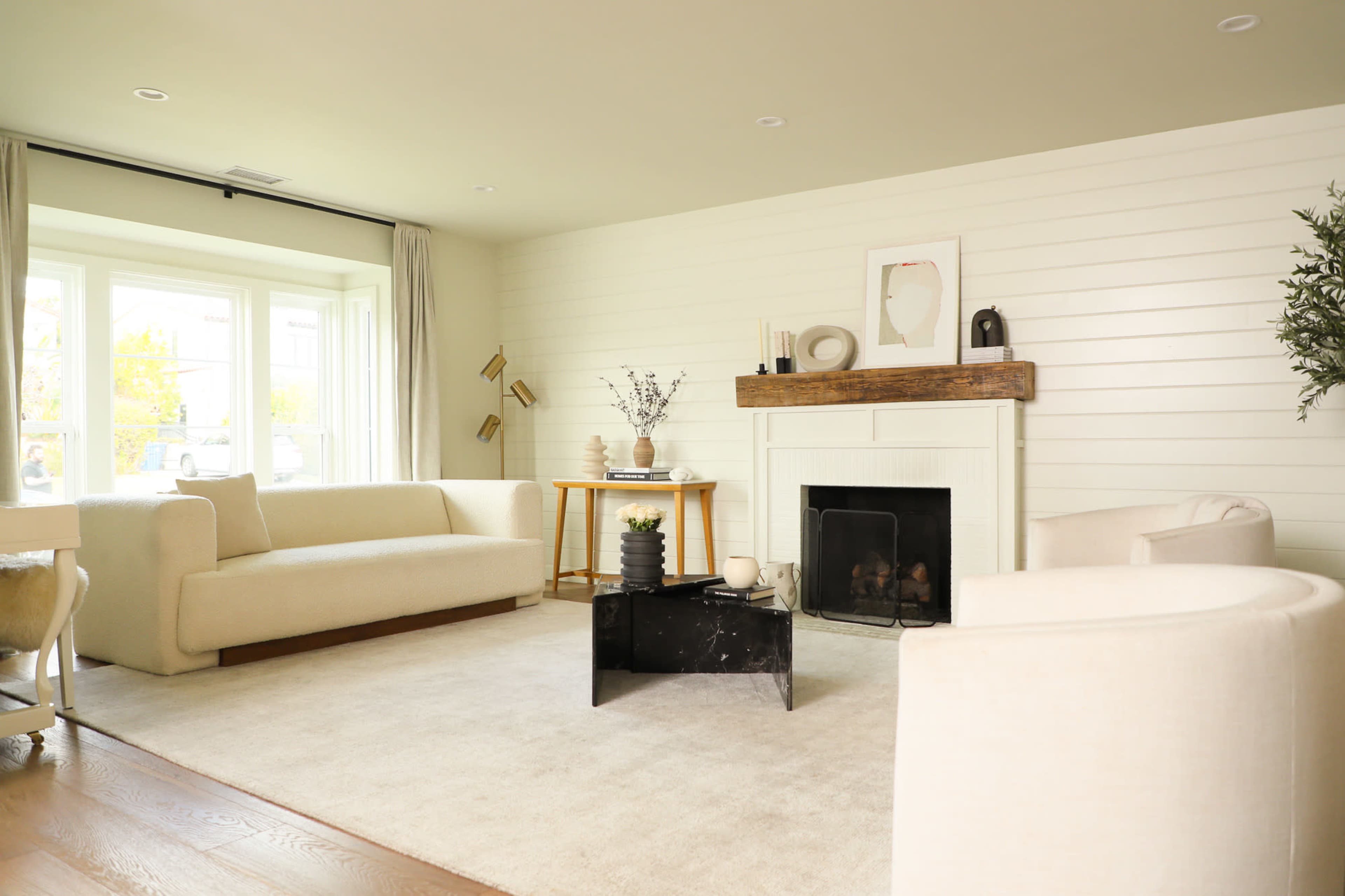 The living room features a light-colored sofa set, a black coffee table, and a fireplace with a wooden mantle, all arranged on a neutral carpet.
