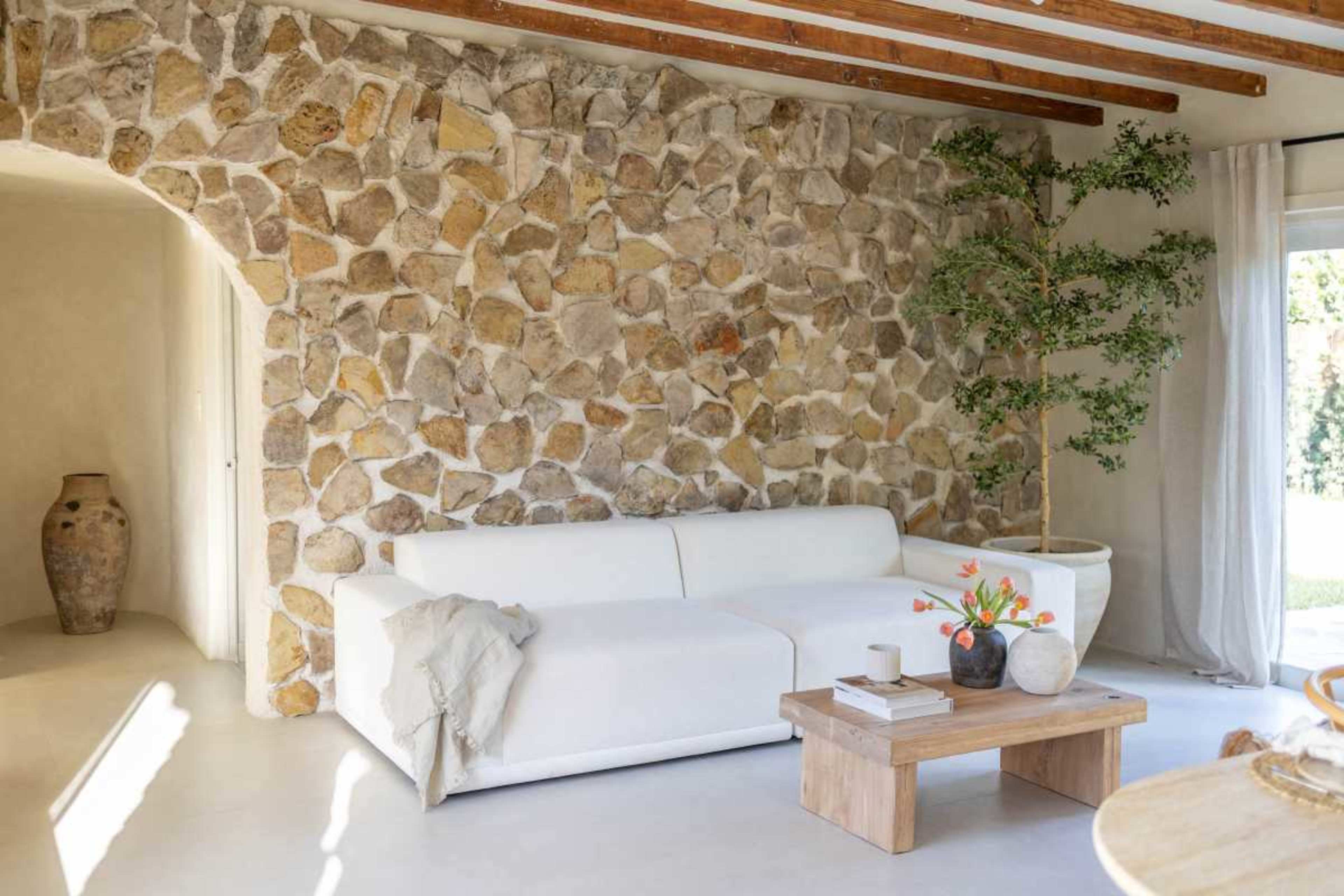 The image shows a modern living room featuring a white sofa, a wooden coffee table, and a textured stone wall.