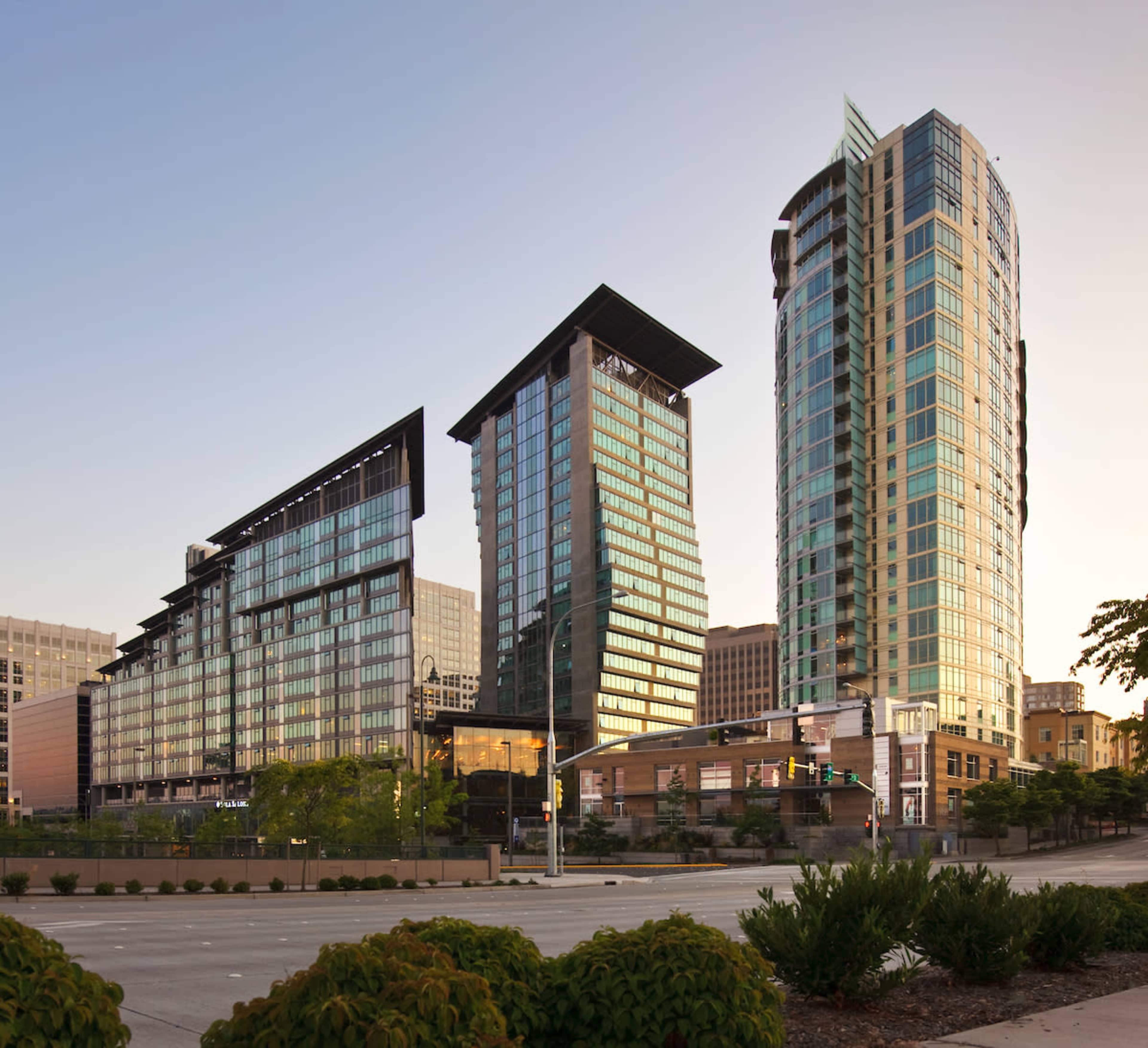 The image shows a modern urban landscape featuring three tower buildings with glass facades, located near a street intersection.