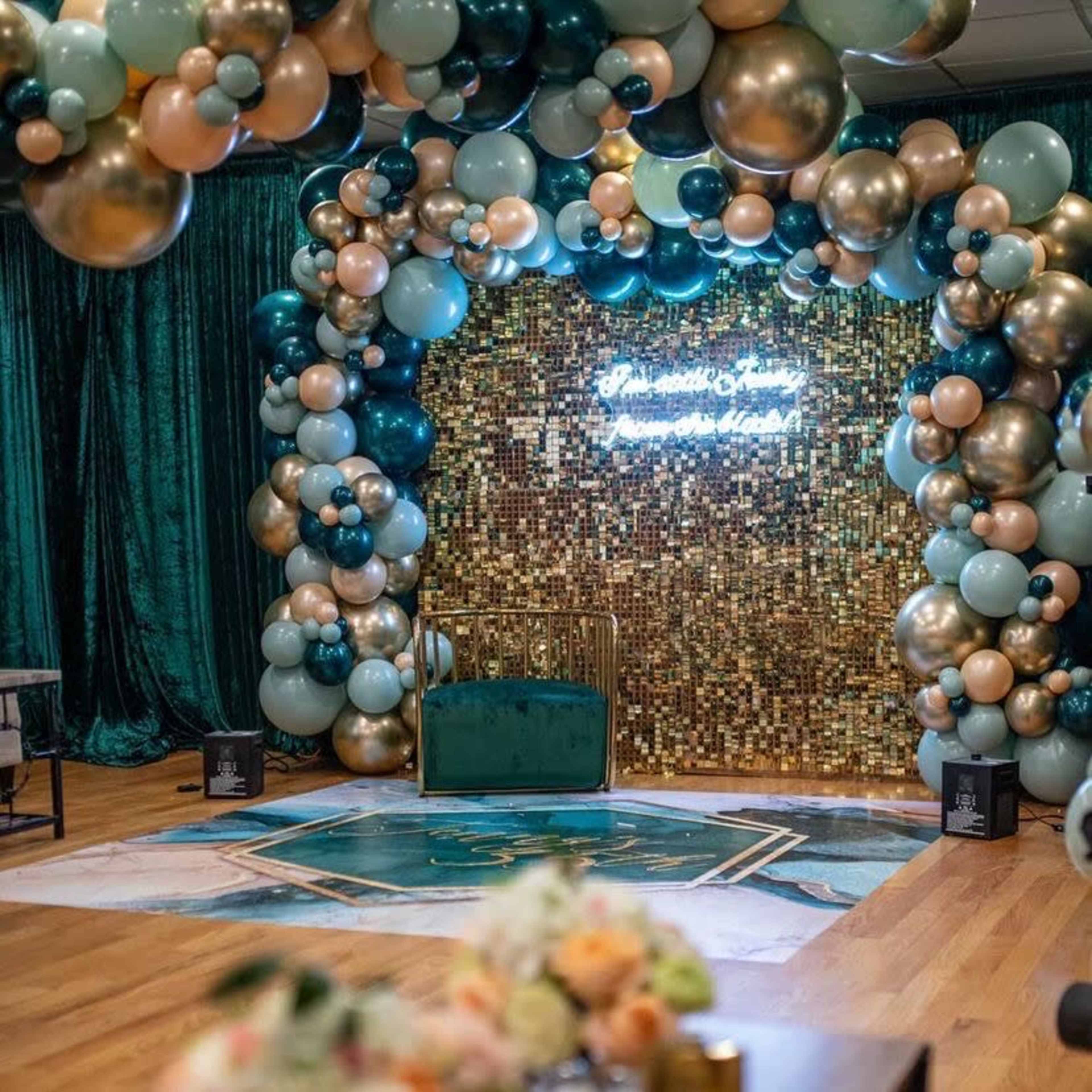 A decorated event space featuring an arch of balloons and a sequin backdrop with a green sofa in front.