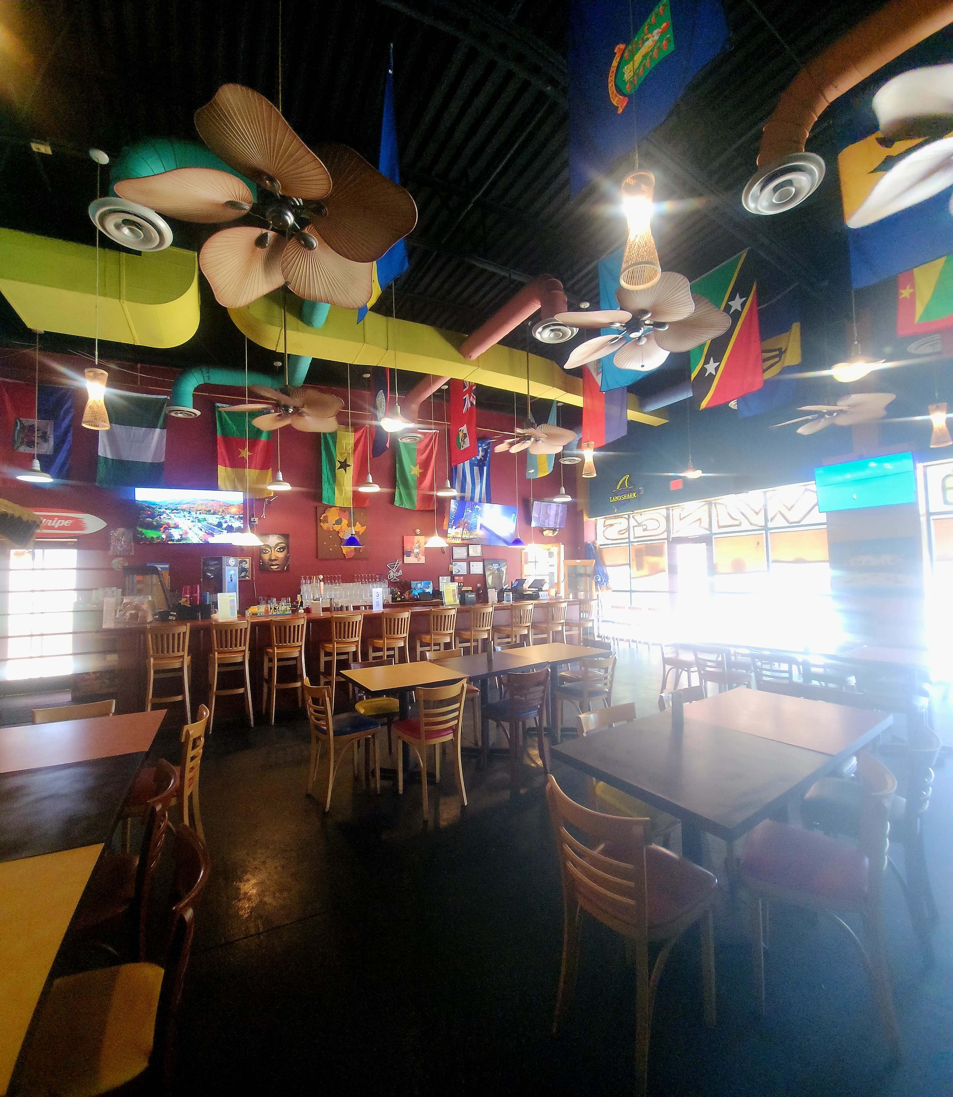 The image shows a lively restaurant interior featuring colorful flags hanging from the ceiling, wooden tables, and a bar area.