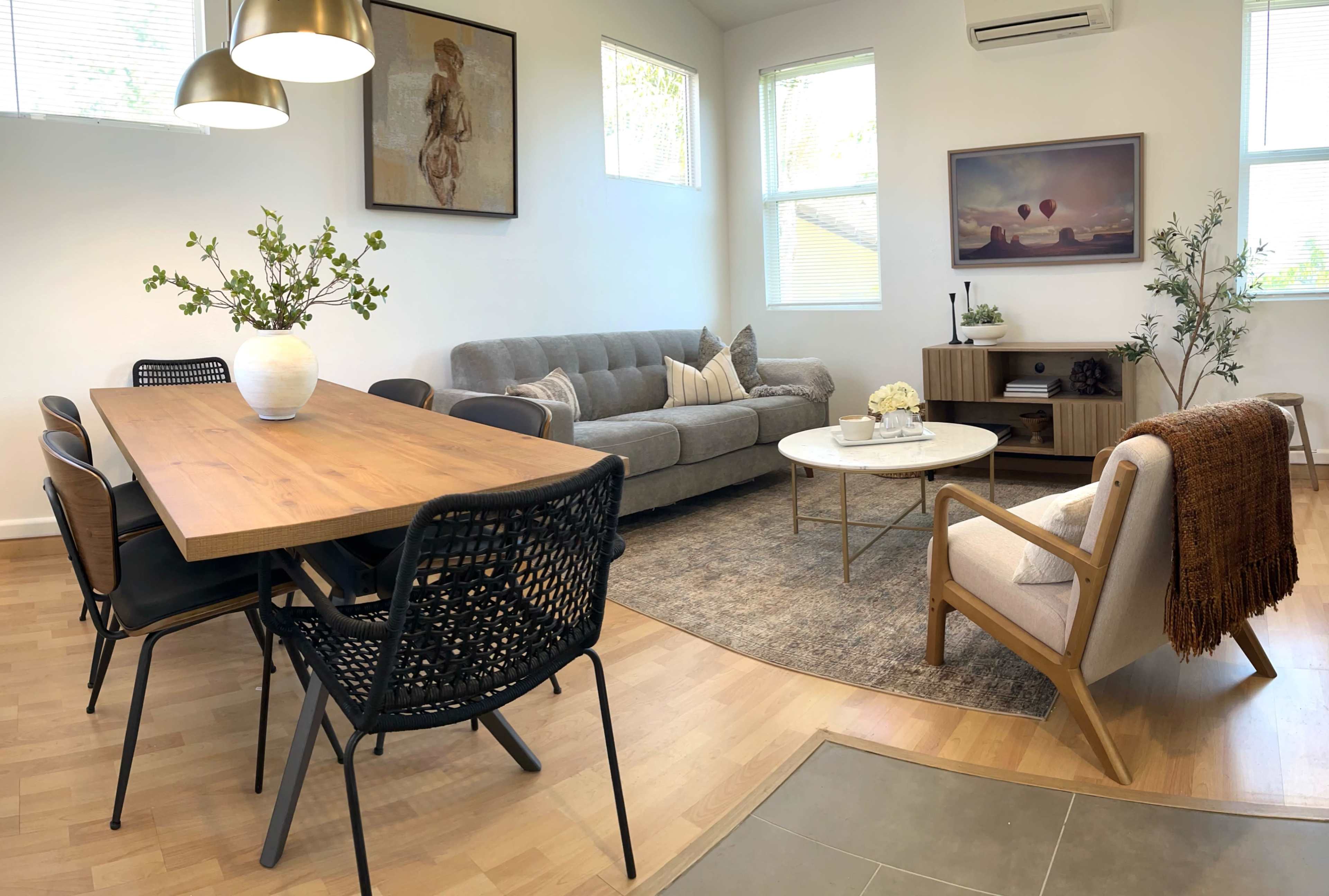 A modern living and dining area featuring a wooden dining table, six black chairs, a gray sofa, a circular coffee table, and decorative artwork on the walls.