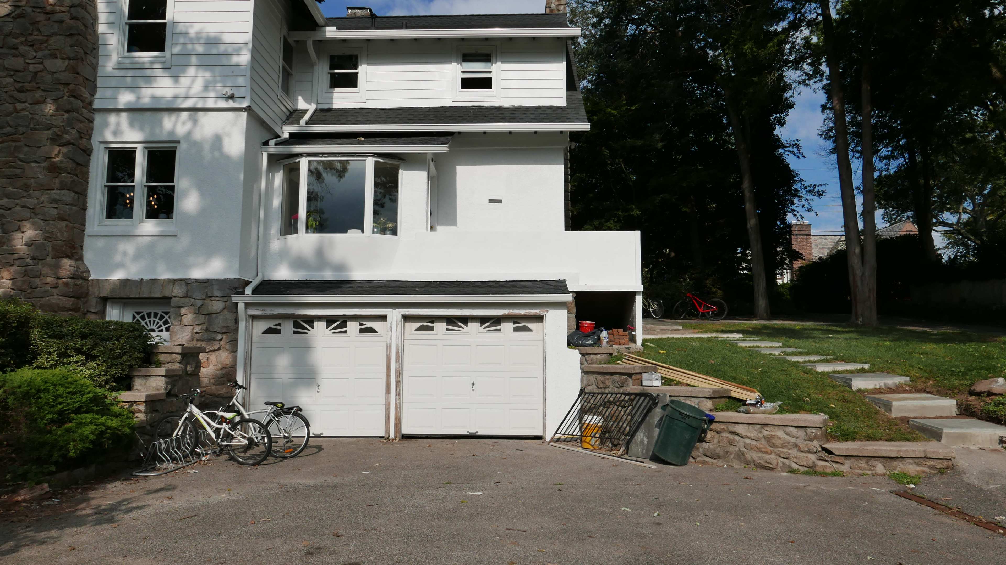 A residential building features a two-car garage with bicycles leaning against it, surrounded by a landscaped area and steps leading to the yard.