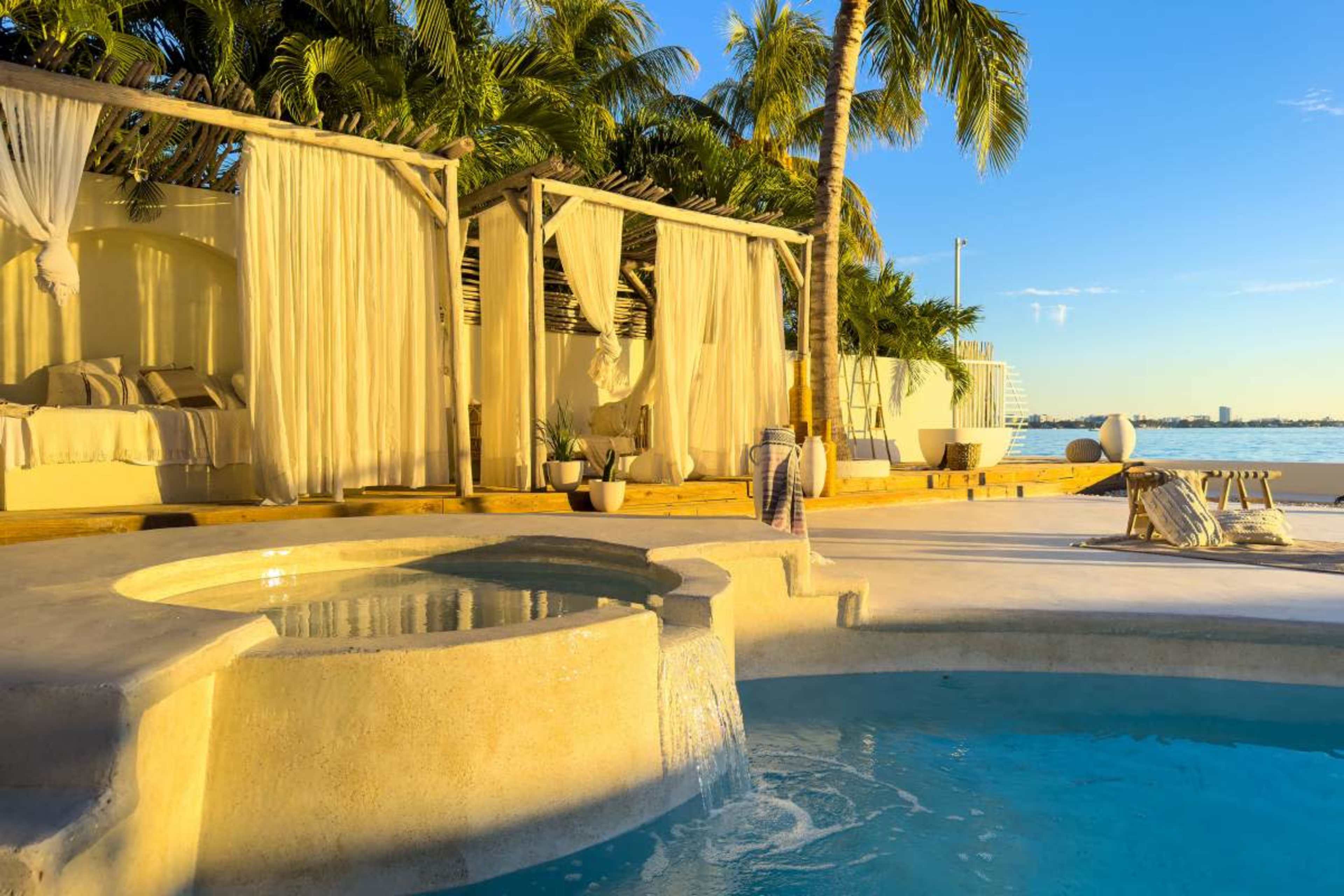 The image features a tranquil outdoor space with a jacuzzi and a swimming pool surrounded by palm trees and lounge areas.