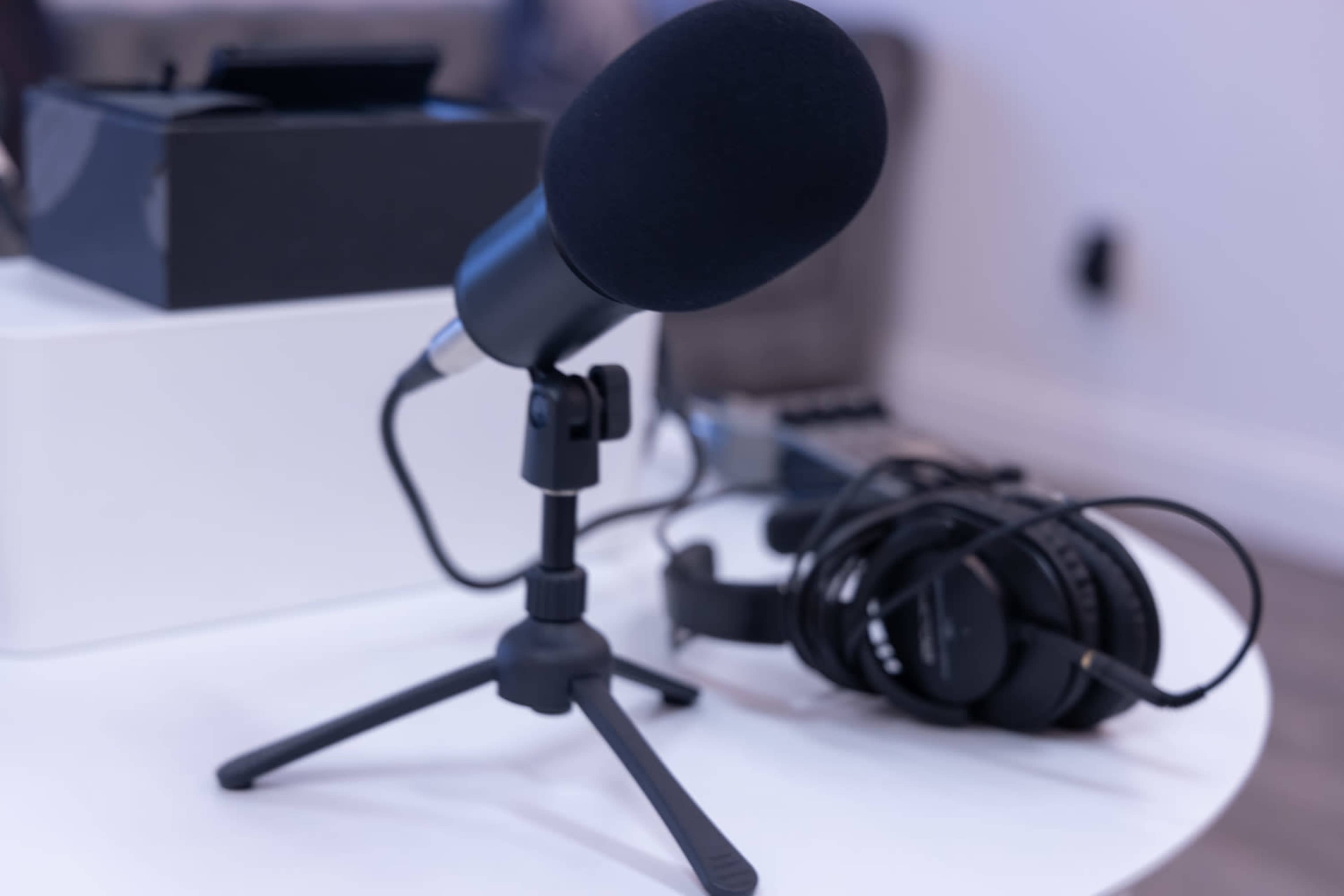 A microphone on a small tripod stand is placed on a table next to a coil of headphones and audio equipment.