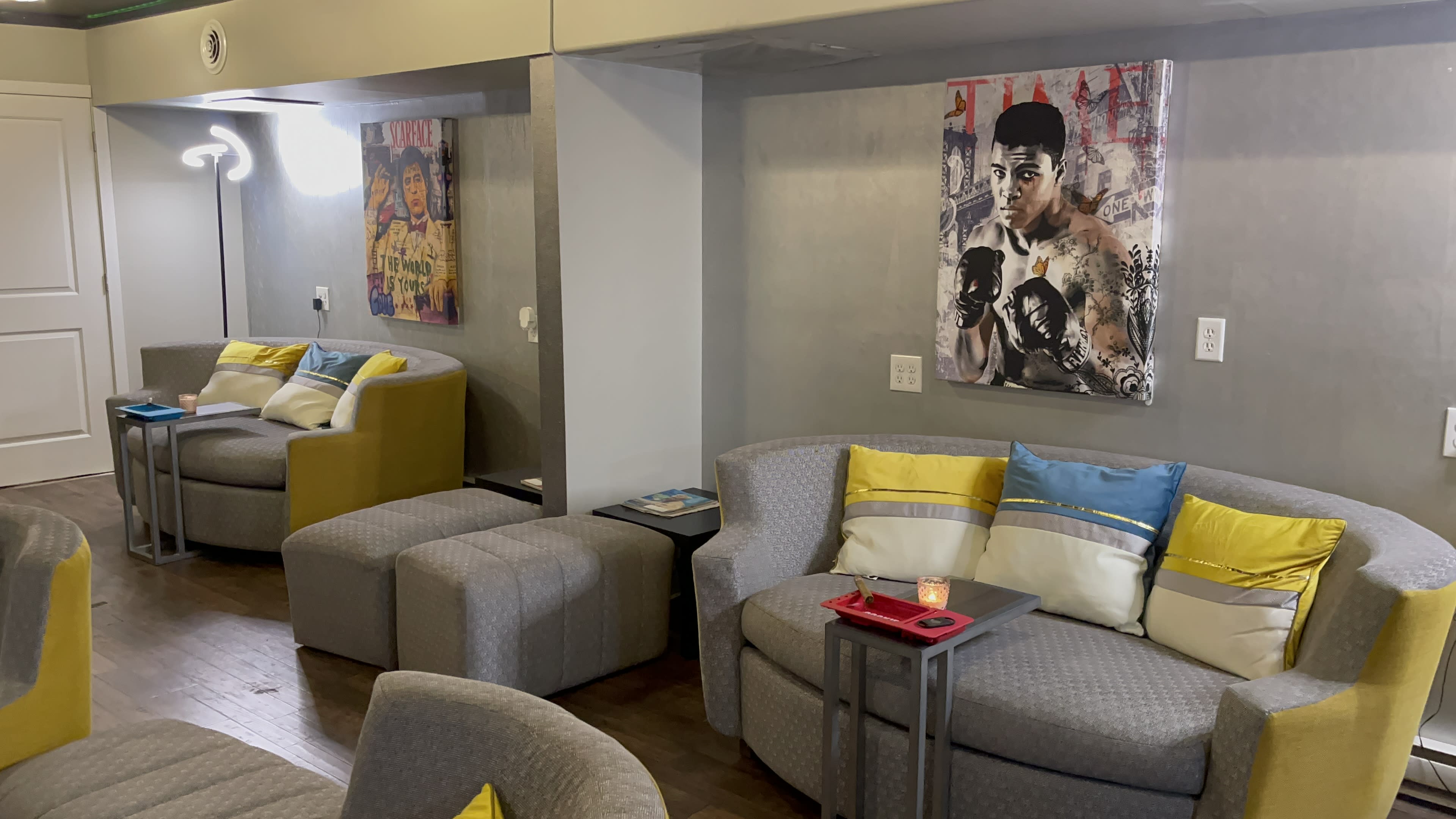The room features seating areas with gray sofas and yellow-accented chairs, alongside wall art depicting a boxer.