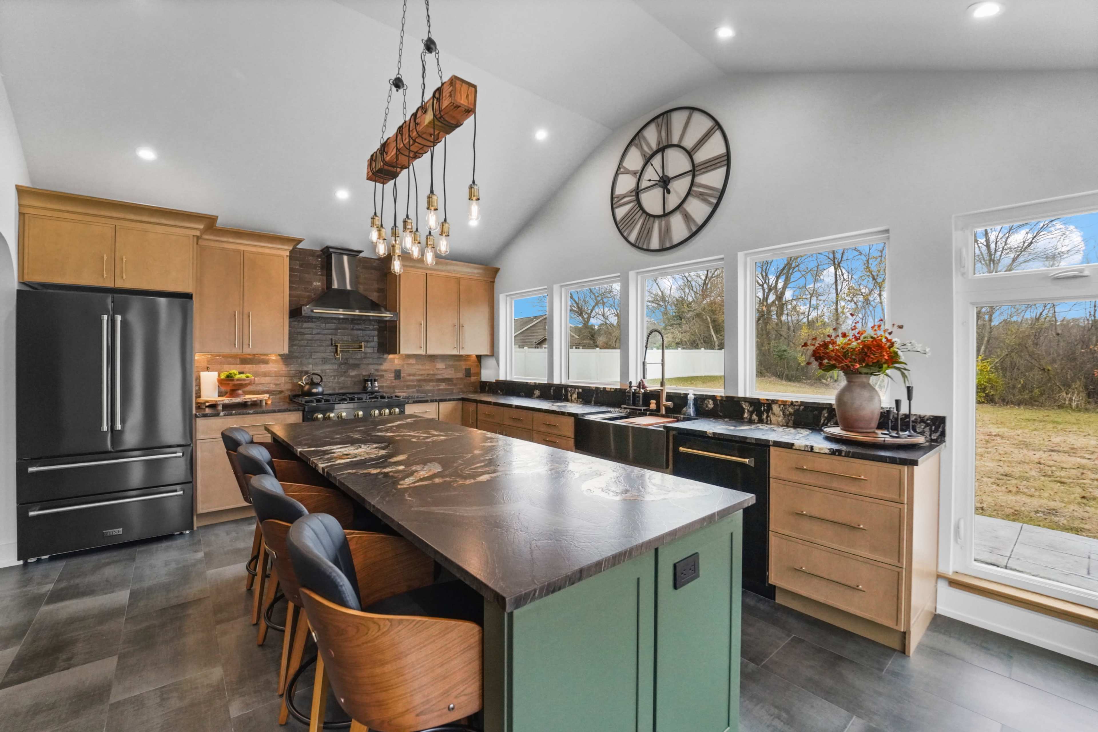 The kitchen features an island with seating, wooden cabinets, and large windows overlooking a yard.