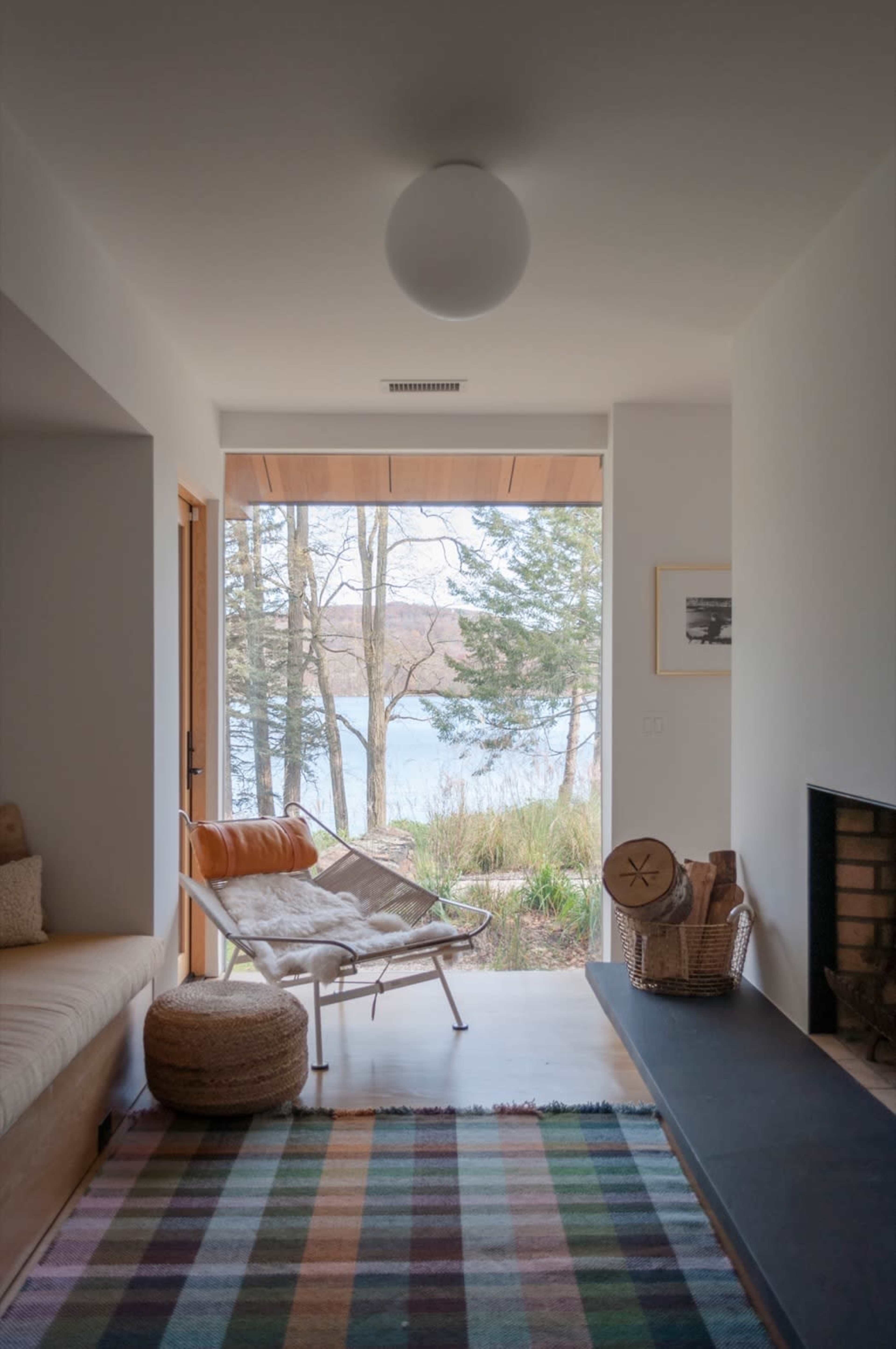 A bright living room features a striped rug, a chair with an orange cushion, and a view of a lake through large windows.