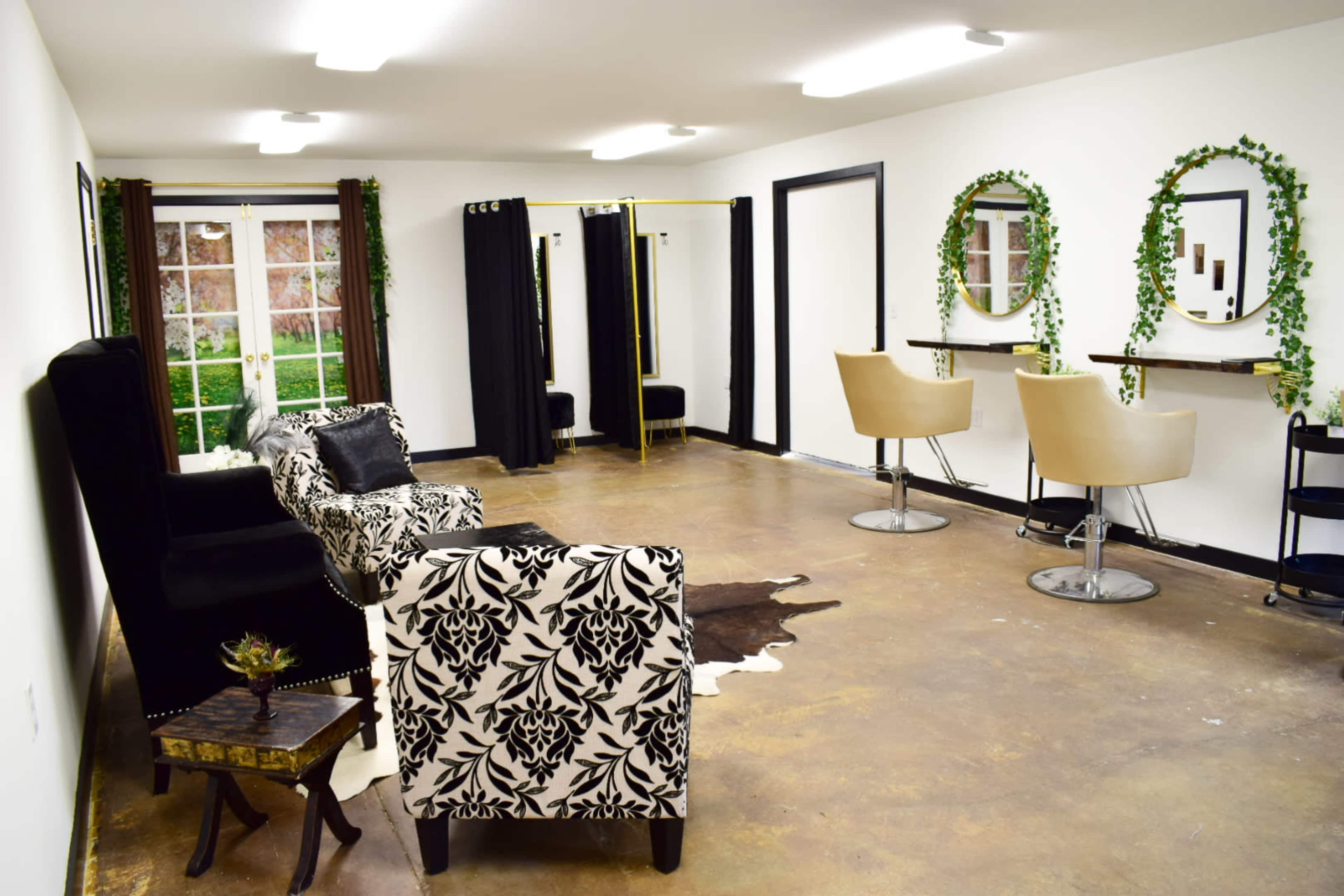 The image shows a spacious salon interior featuring two black and white chairs, a bar area with two stools, and mirrors adorned with greenery.