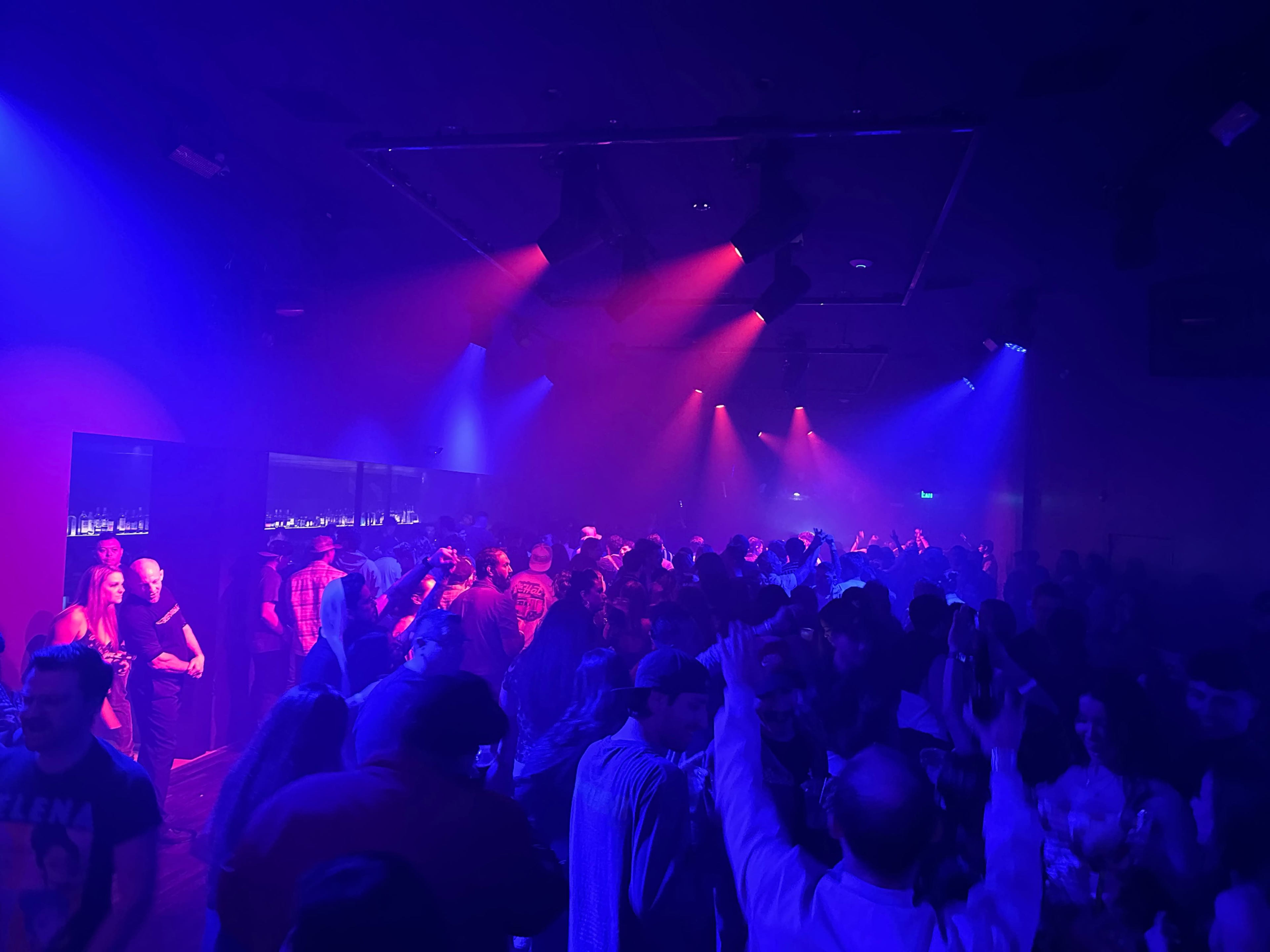 A crowd of people dances under vibrant blue and red lights in a lively nightclub.