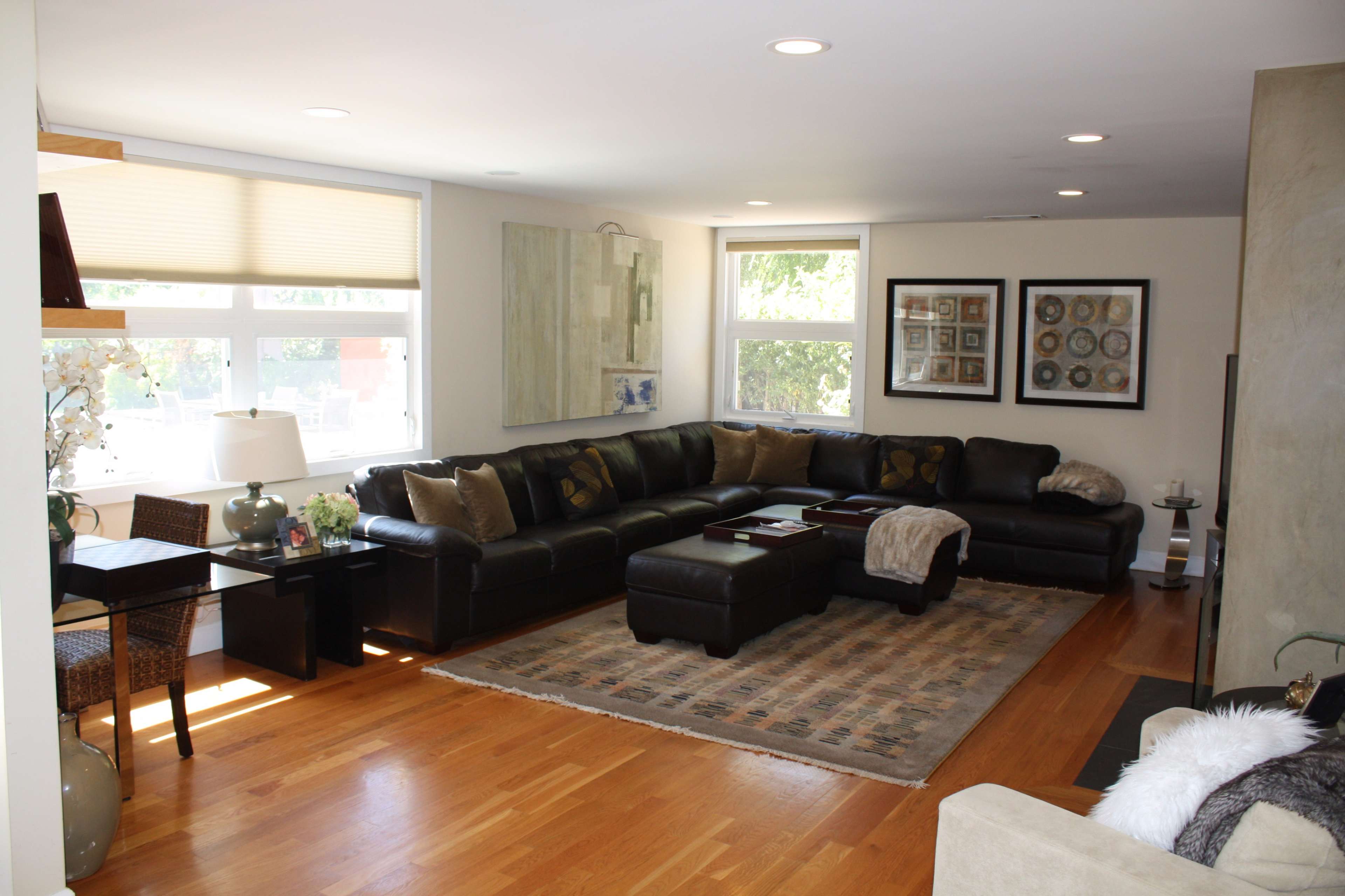 A living room featuring a black sectional sofa, wooden flooring, and a variety of decorative art on the walls.