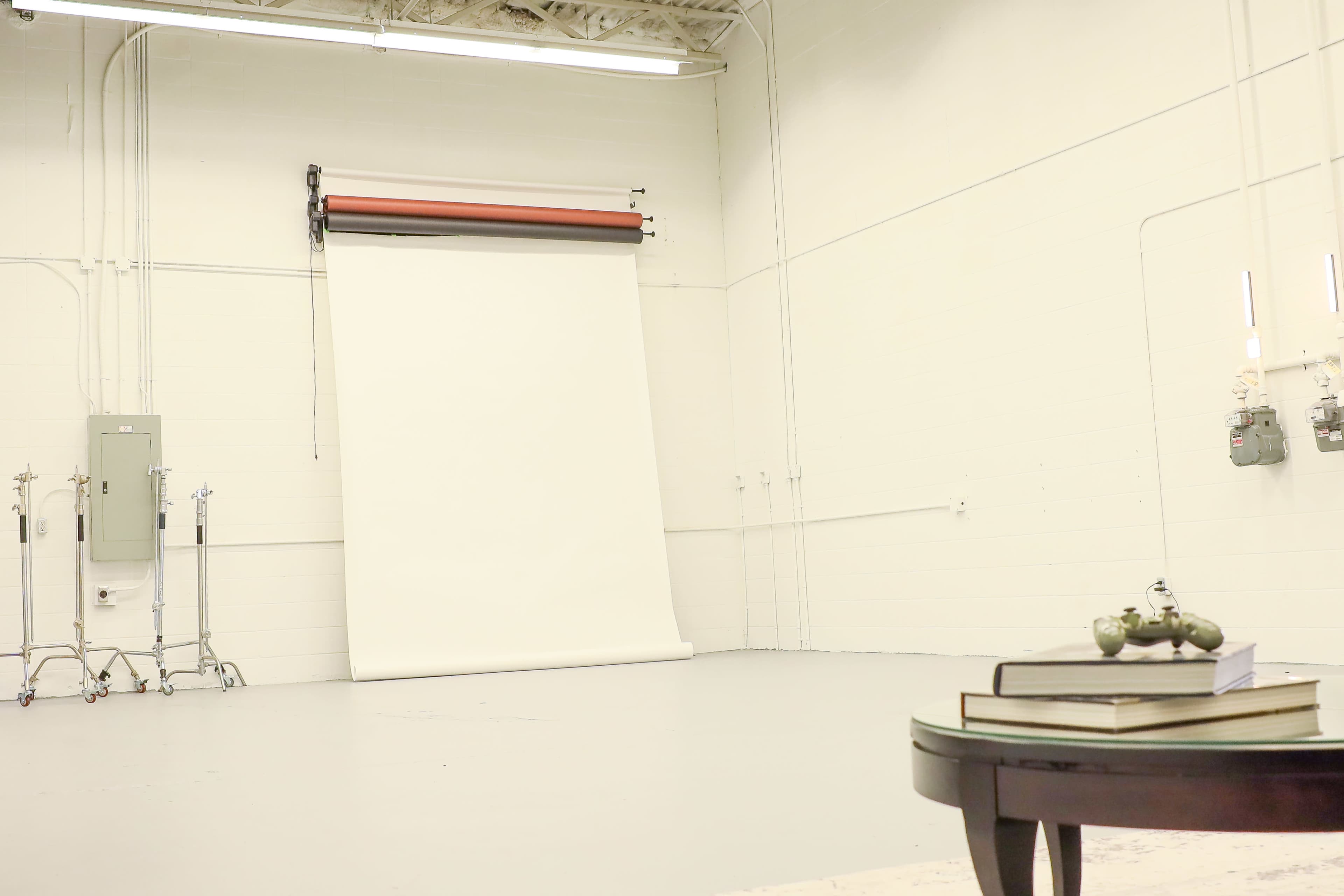 A spacious, empty photography studio with a white backdrop and a small table with books in the foreground.