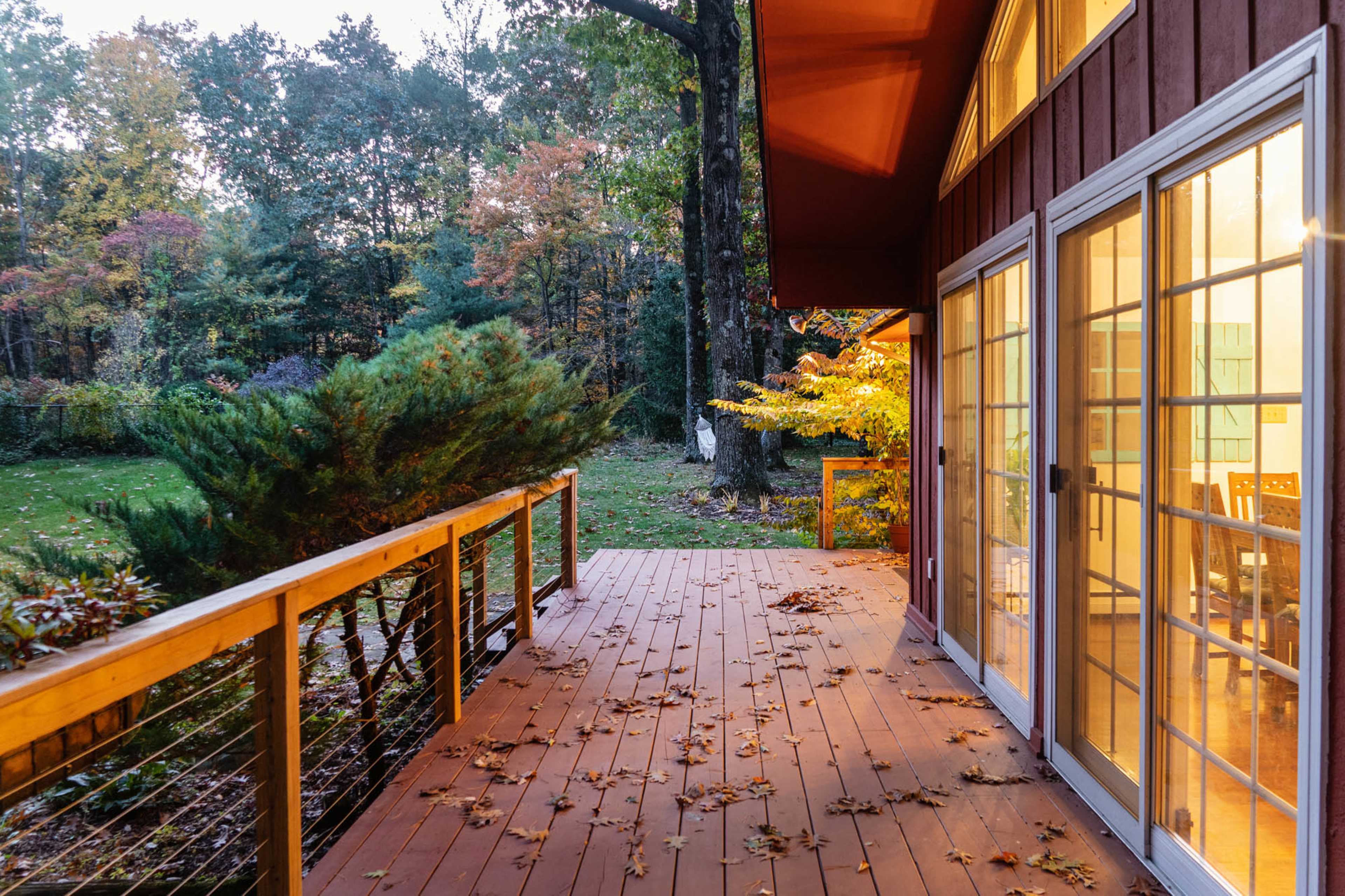 A wooden deck with fallen leaves overlooks a green yard surrounded by trees in the evening light.