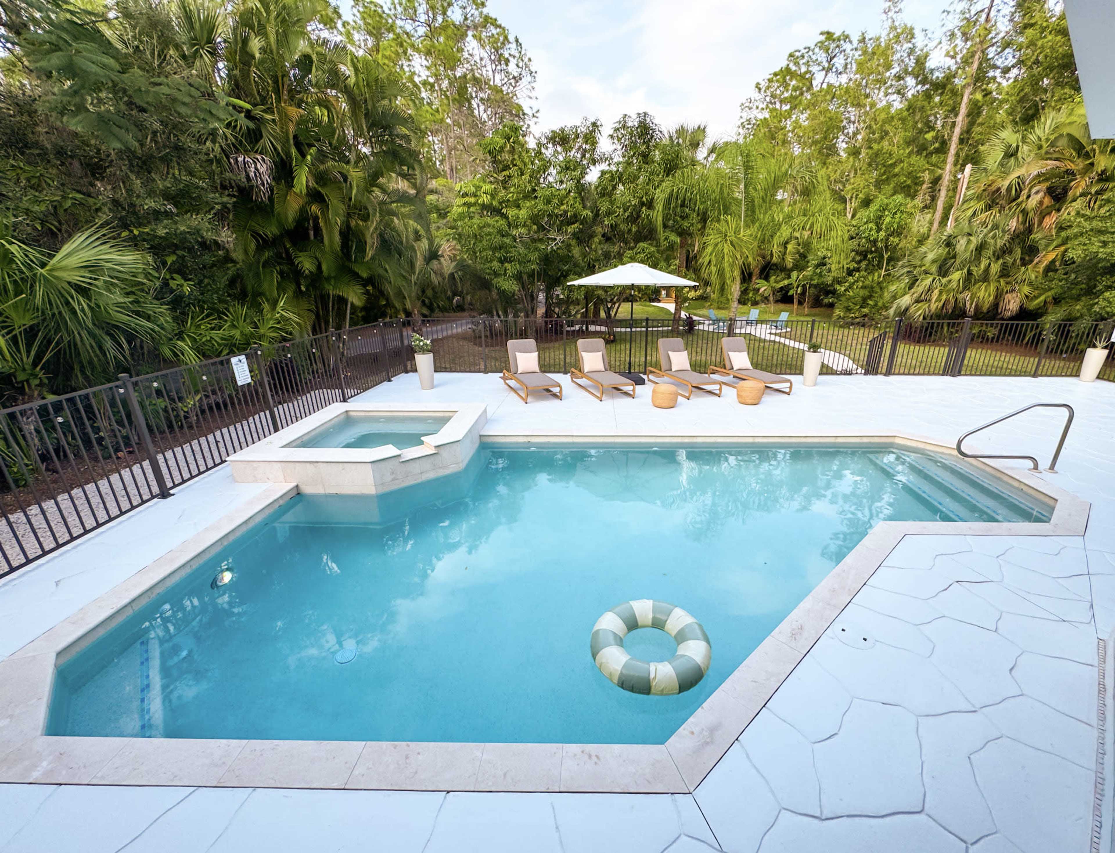 The image shows a rectangular swimming pool with a whirlpool section, surrounded by loungers and lush greenery.