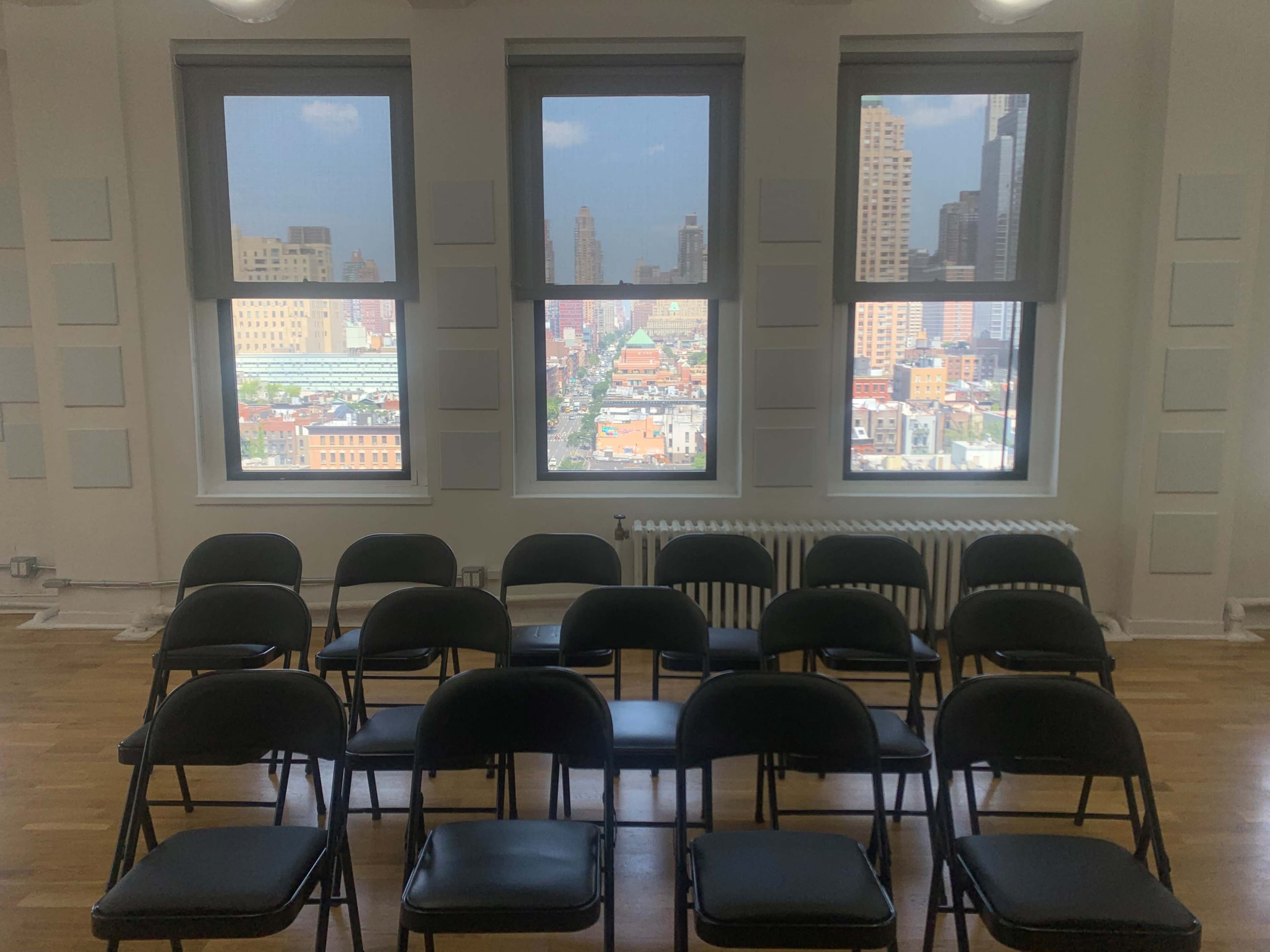A row of black chairs arranged in front of large windows overlooking a cityscape.