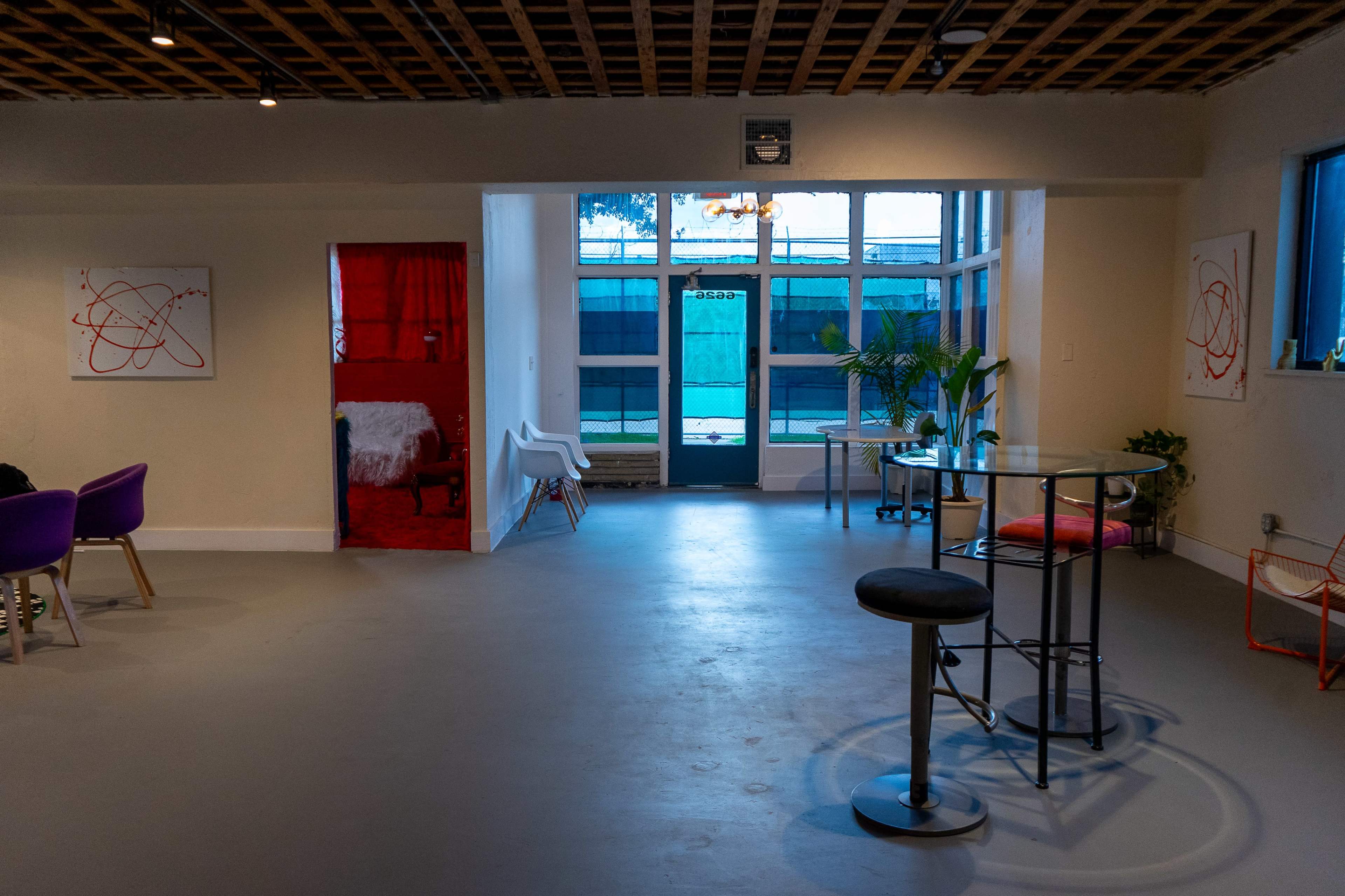 The image shows a spacious, modern interior with a mixture of seating areas, decorative artwork on the walls, and large windows allowing natural light to enter.