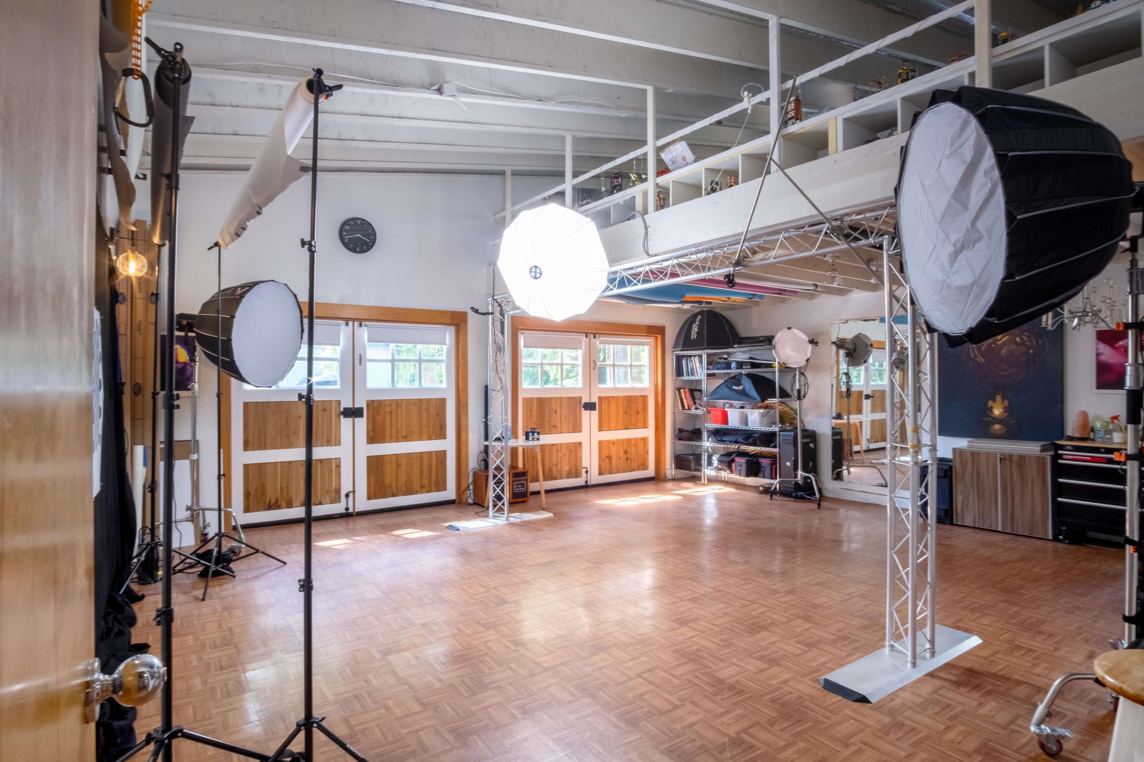 A photography studio with lighting equipment and a lofted area, featuring wooden doors and a polished floor.