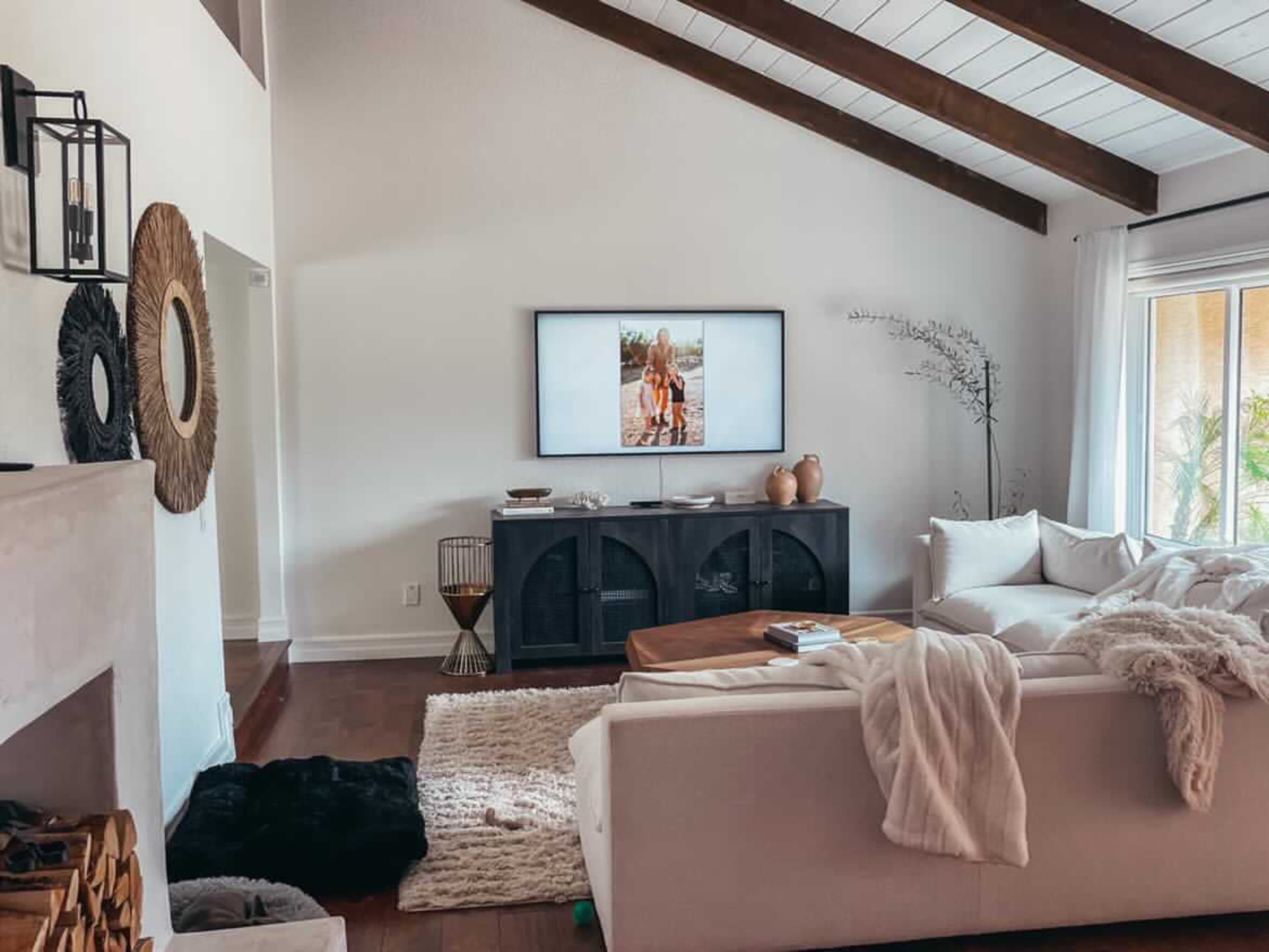 A cozy living room features a white sofa, a wooden coffee table, and a large television mounted on the wall displaying a photograph.