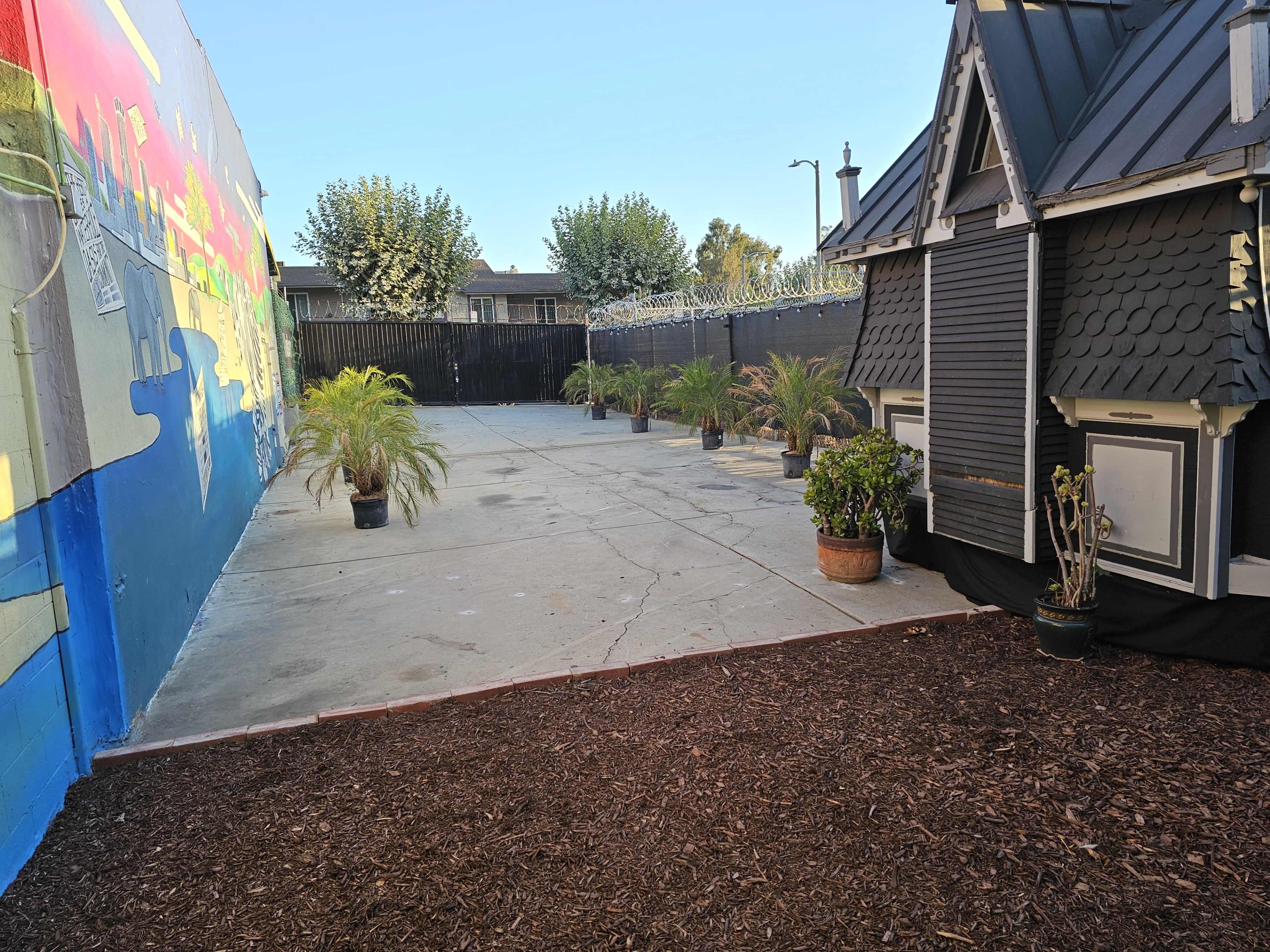 A spacious outdoor area featuring a concrete surface, a mural on one wall, and several potted plants.
