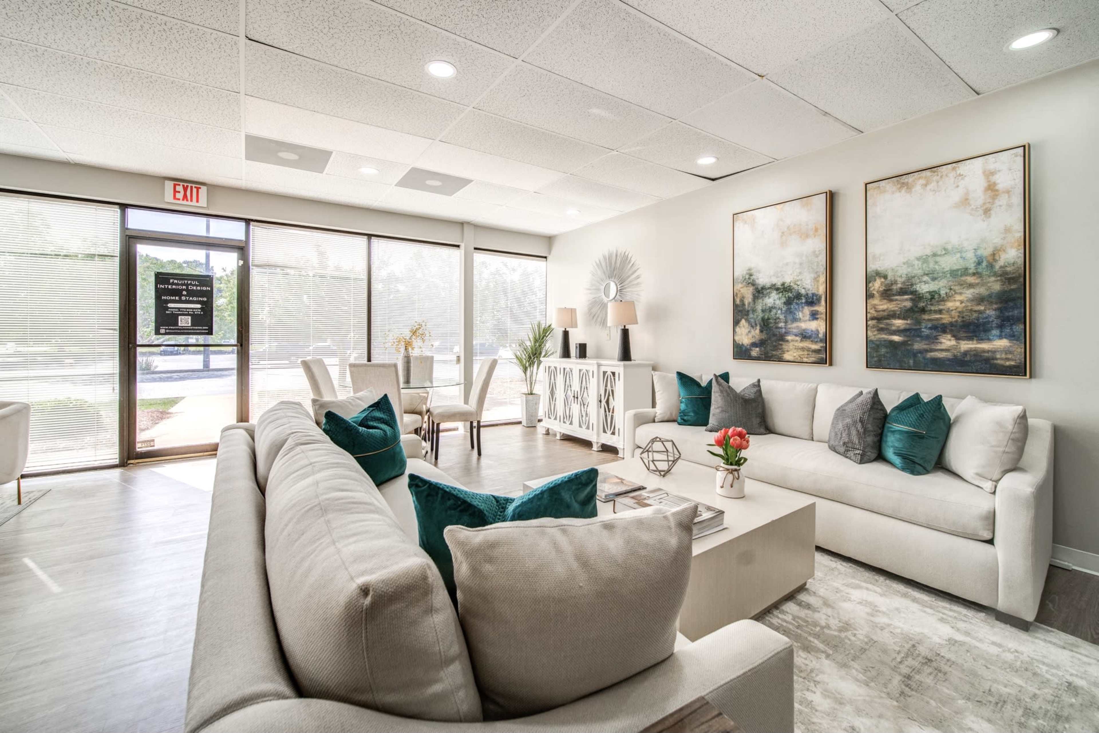 A modern living room features two sofas, decorative throw pillows, a coffee table, and artwork on the walls, with large windows allowing natural light to illuminate the space.