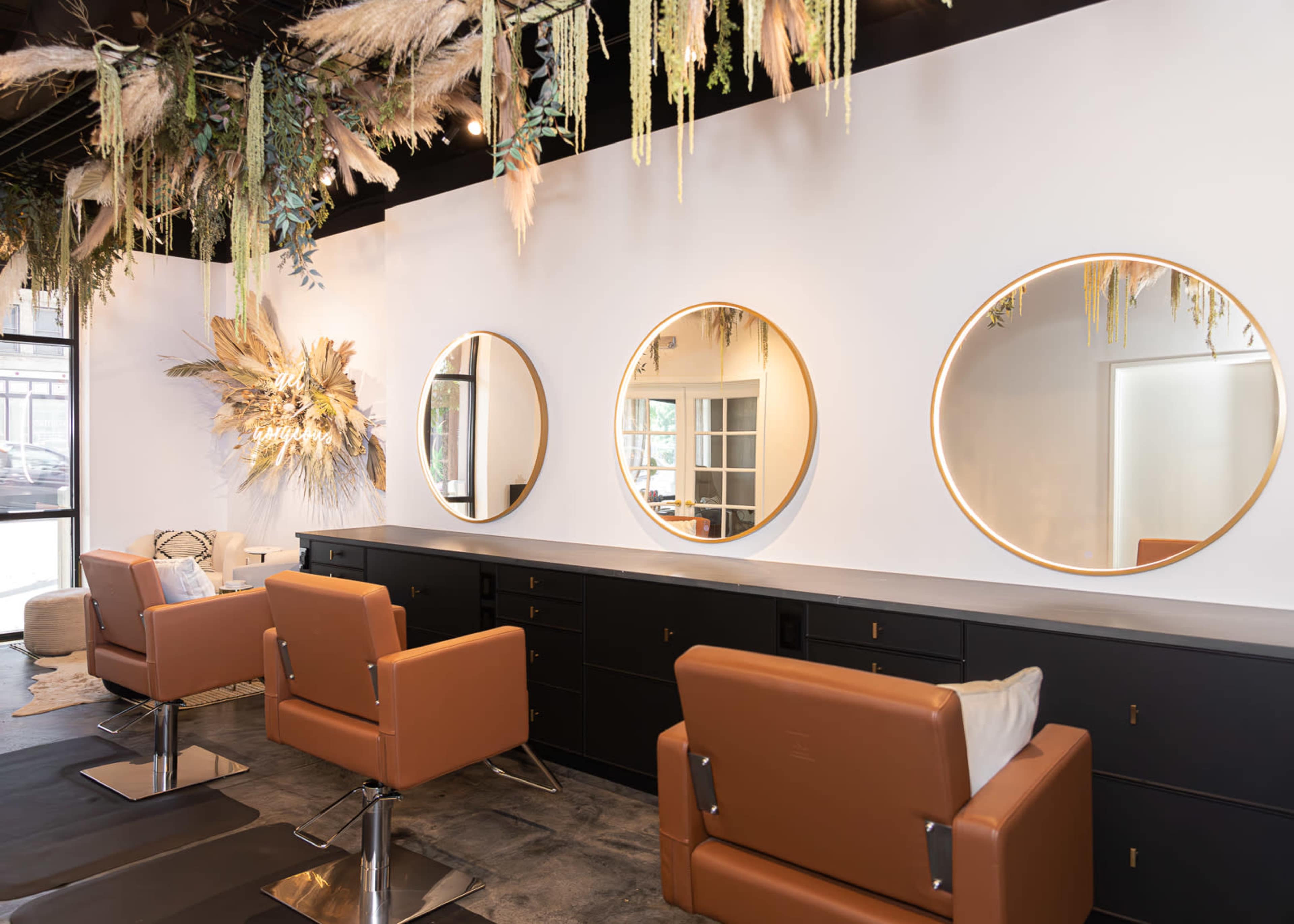 The image shows a modern hair salon with three circular mirrors, styled chairs, and decorative plants hanging from the ceiling.
