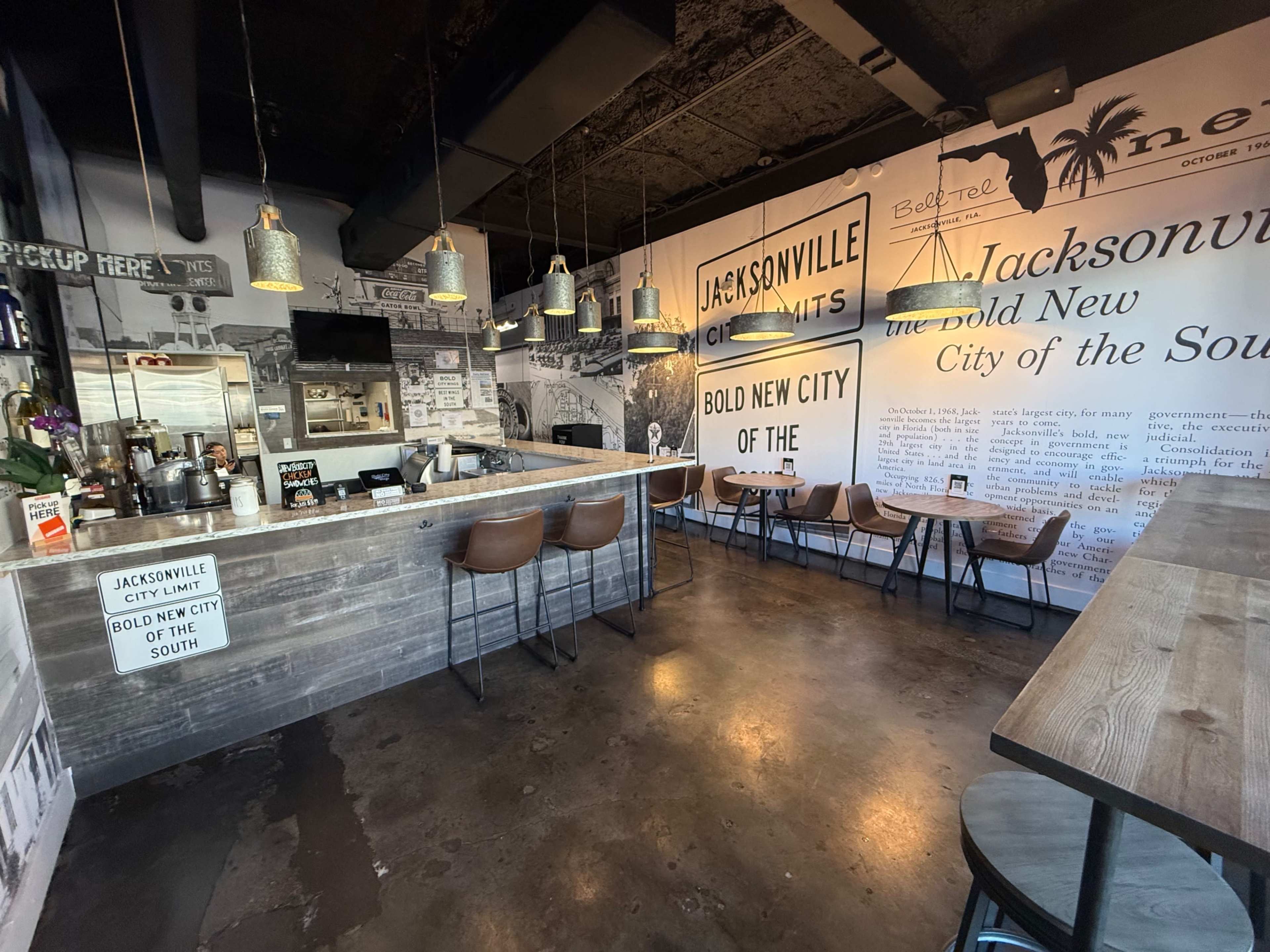 The interior of a cafe features a wooden bar, several tables, and walls adorned with black and white photographs and text about Jacksonville.