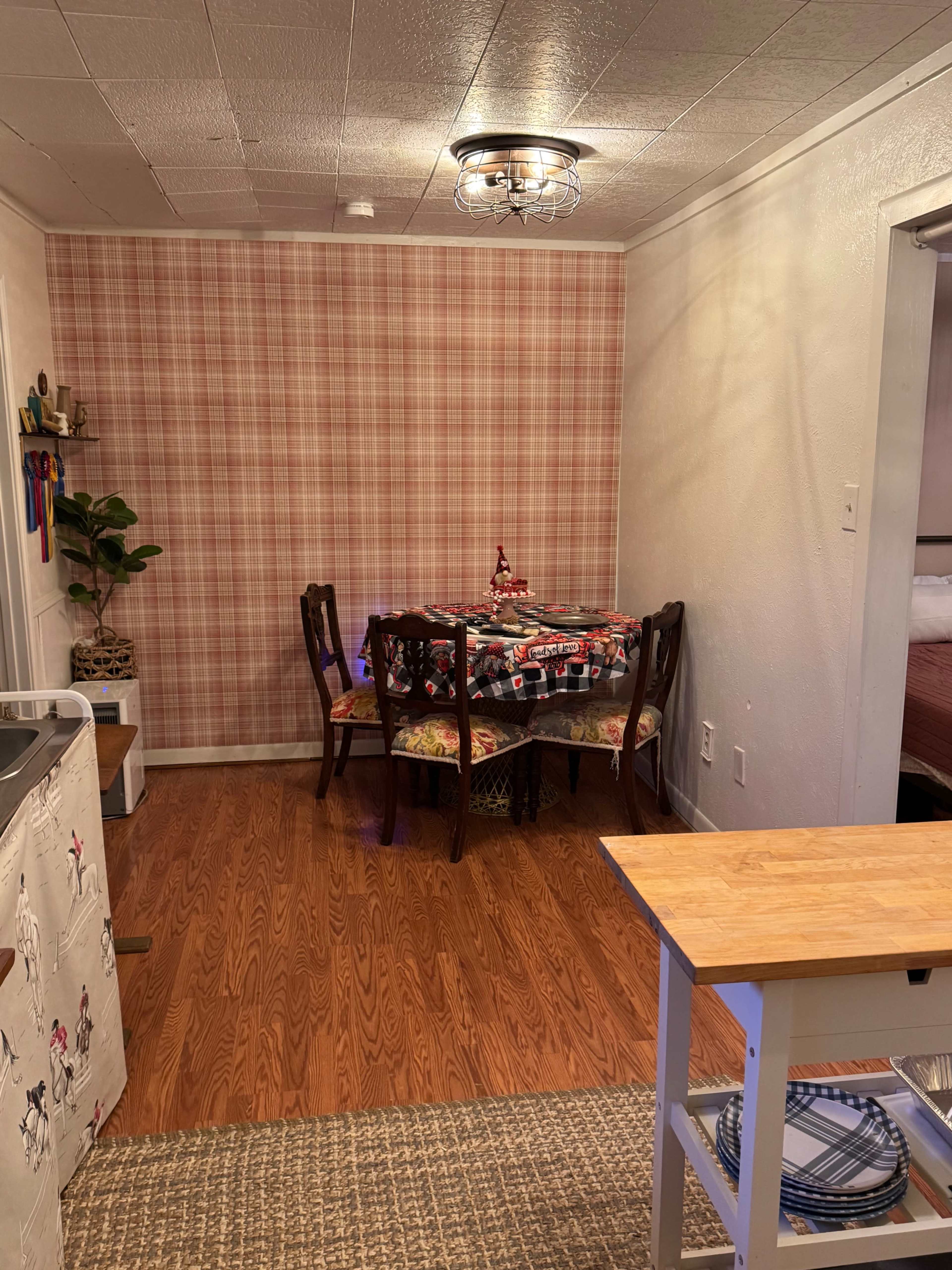 The image shows a small dining area with a table set for four chairs, a patterned wall, and a kitchen counter in the foreground.