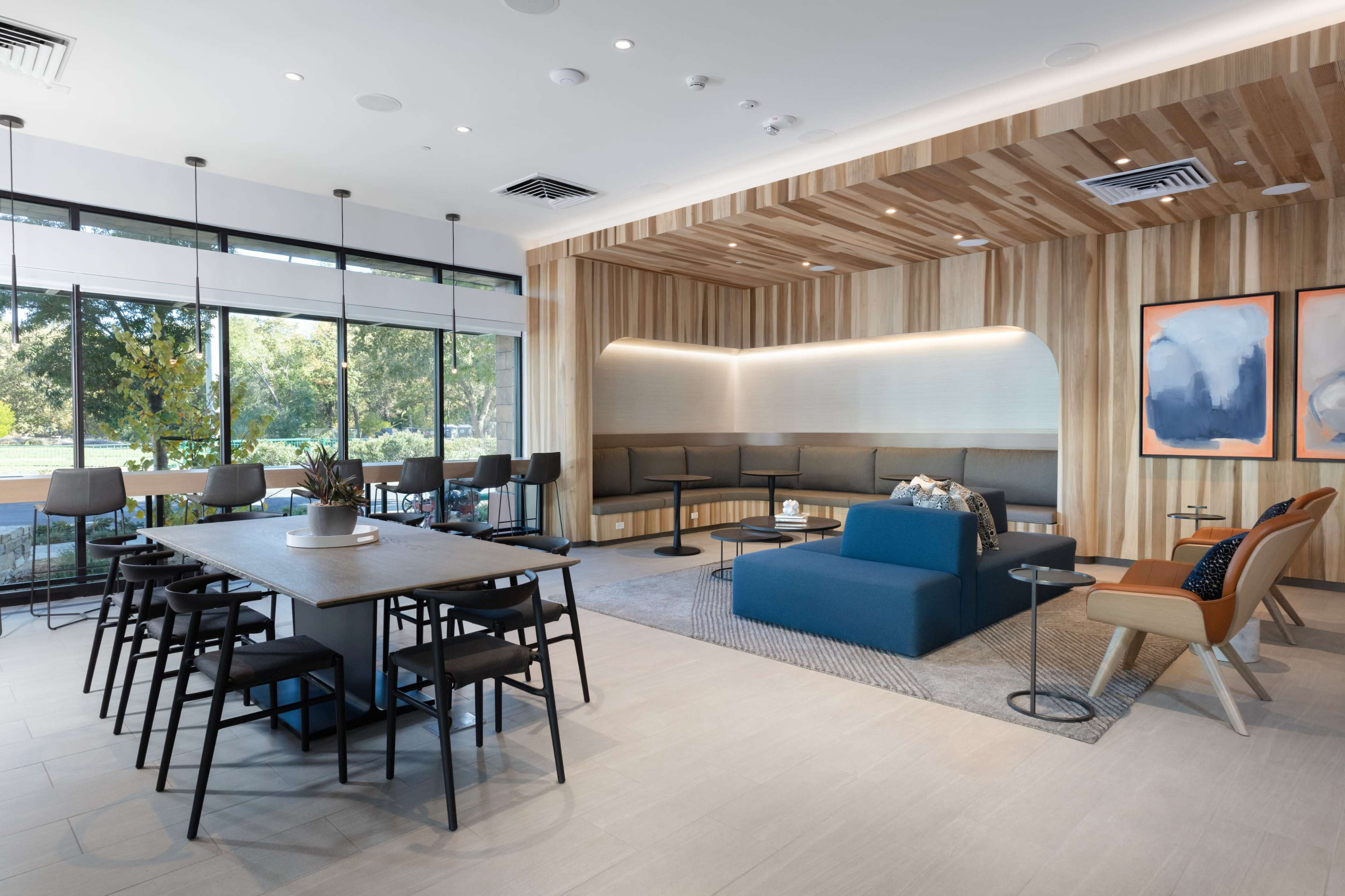 A modern lounge area with a blue seating arrangement, wooden paneling, and a mix of tables and chairs arranged for social interaction.