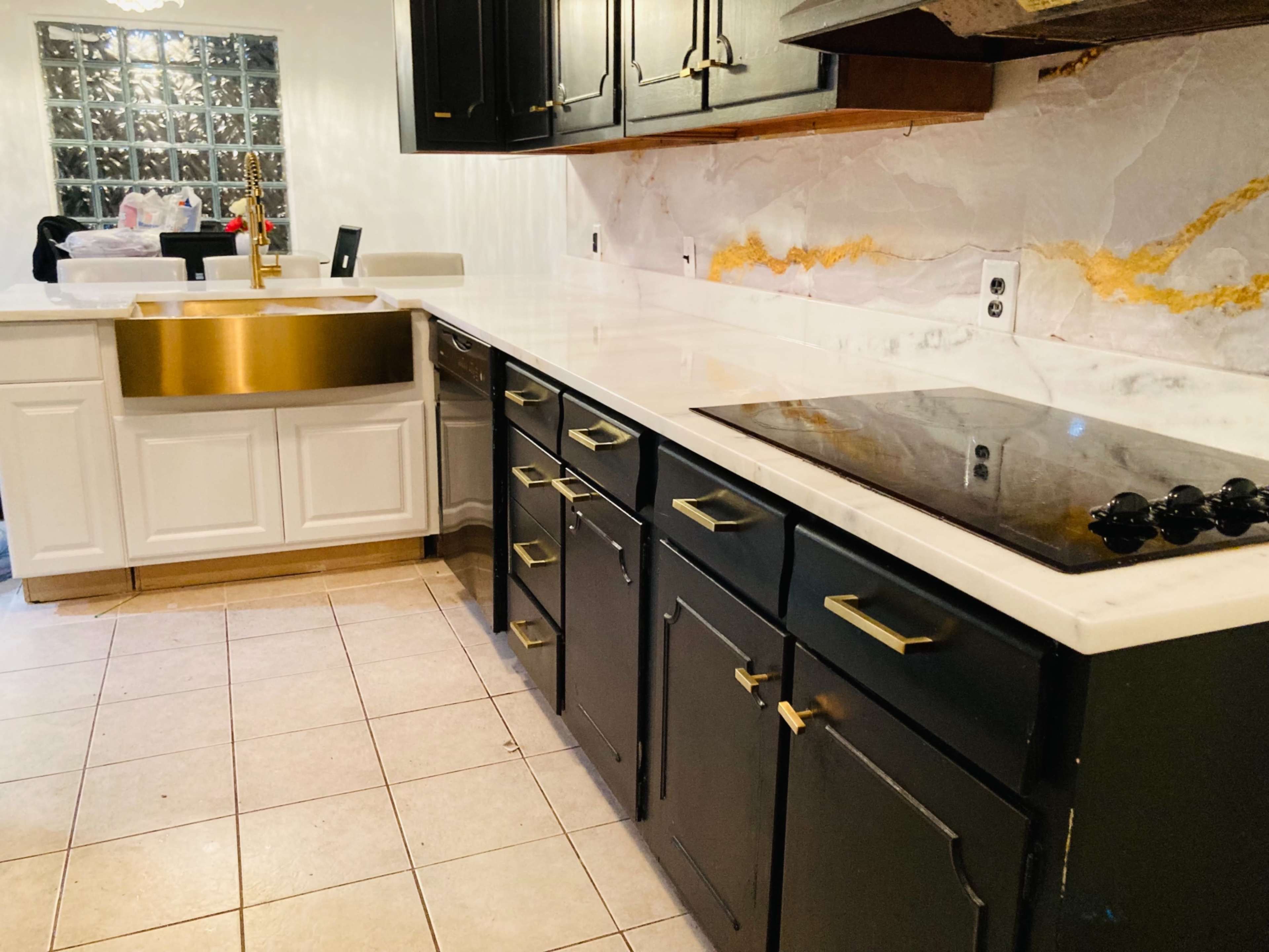 A modern kitchen with black and white cabinetry, a gold sink, and a countertop made of white marble.