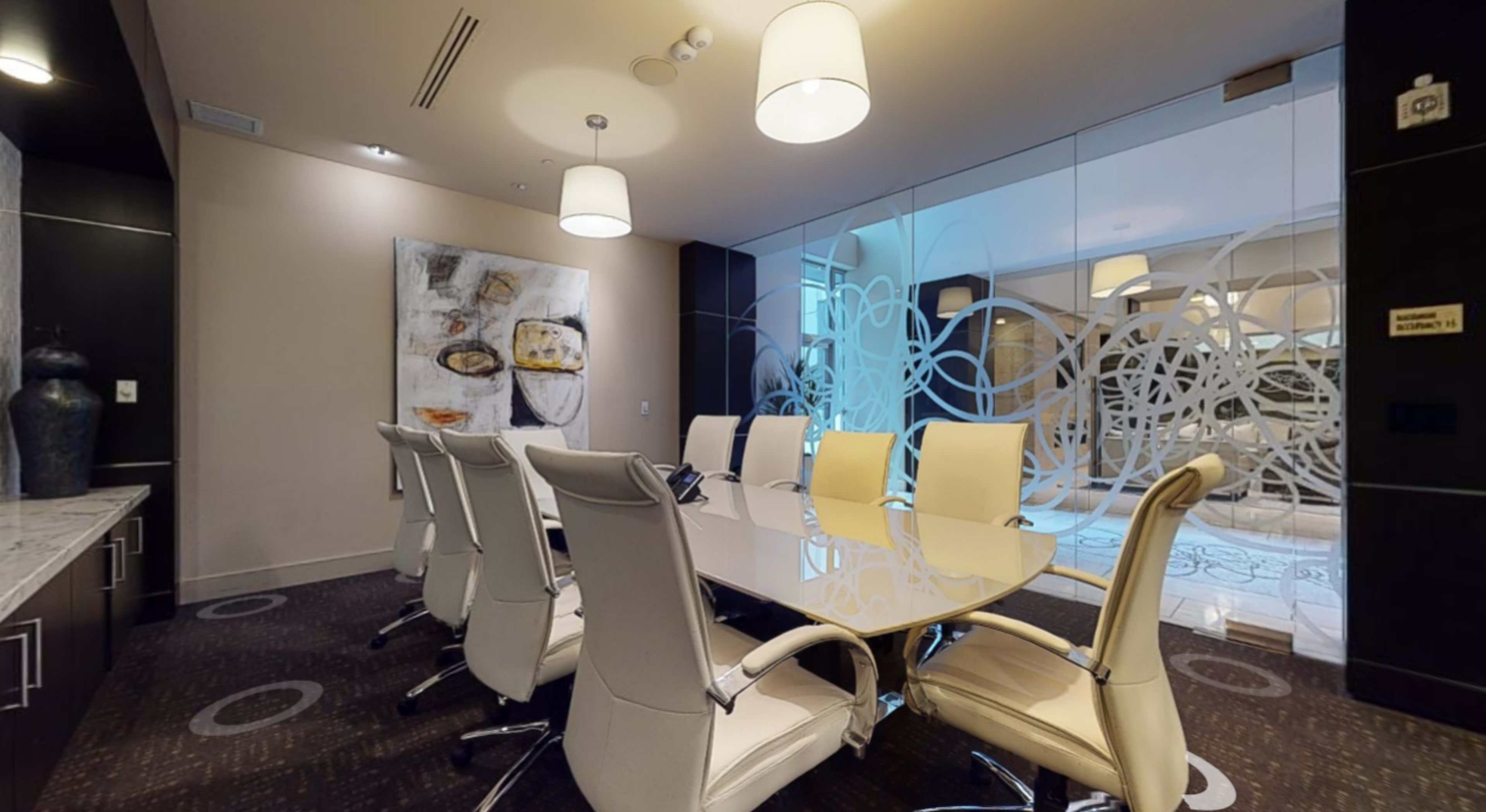 A modern conference room with a long table surrounded by white leather chairs and a glass wall featuring artistic designs.