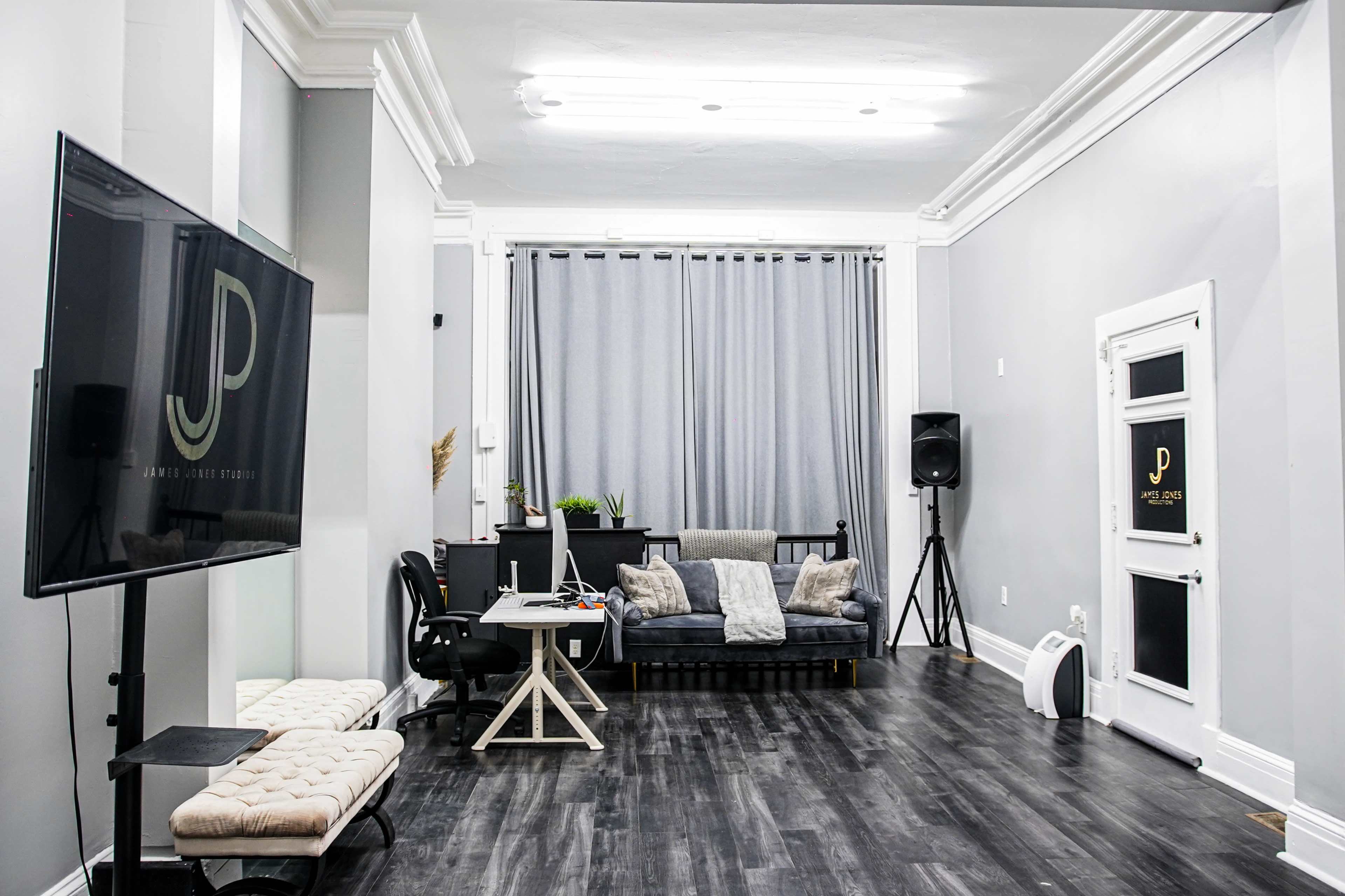 A modern studio features a gray color scheme with a couch, desk, and large screen along one wall.