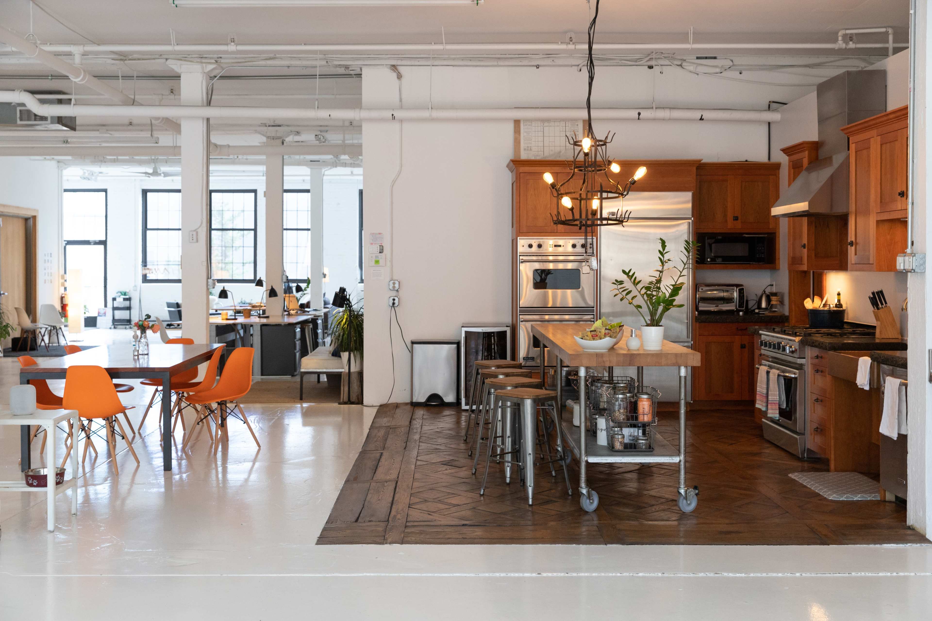 A spacious kitchen features wooden cabinetry, a large island with stools, and a dining area with modern chairs, surrounded by an open layout office space.