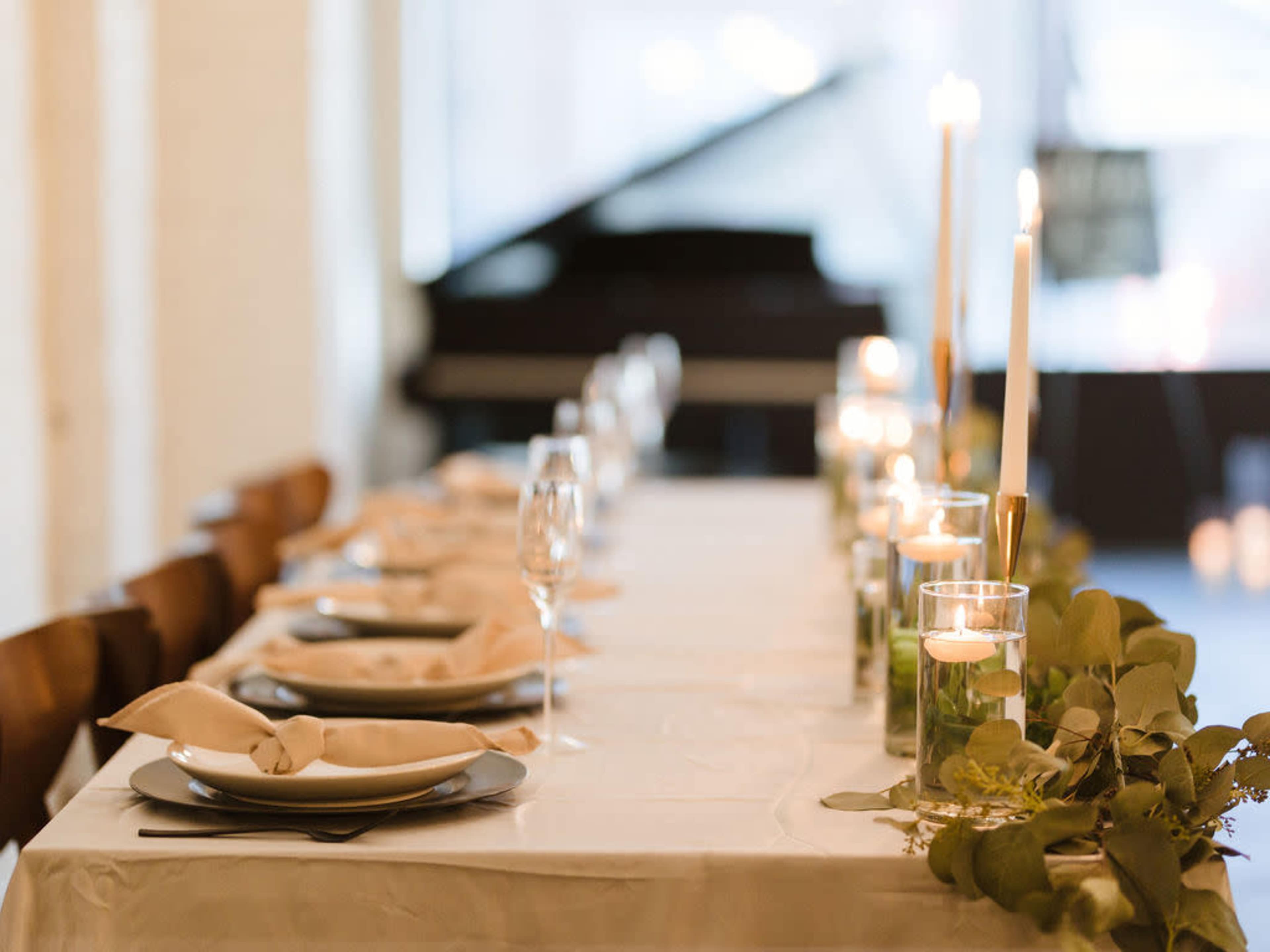 A long dining table is set with plates, glasses, and candles, alongside a piano in the background.