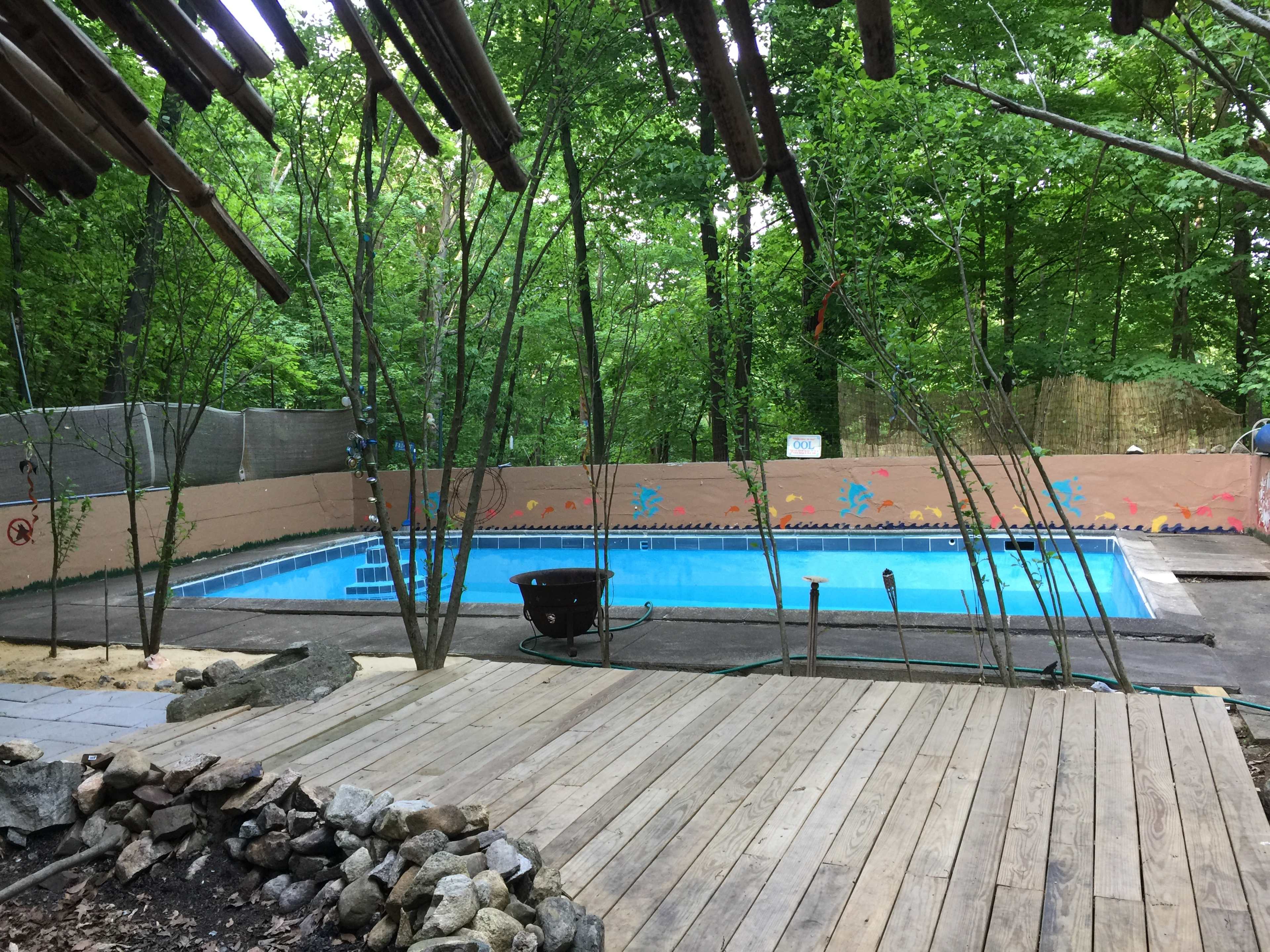 A swimming pool sits surrounded by trees and wooden decking in a wooded area.