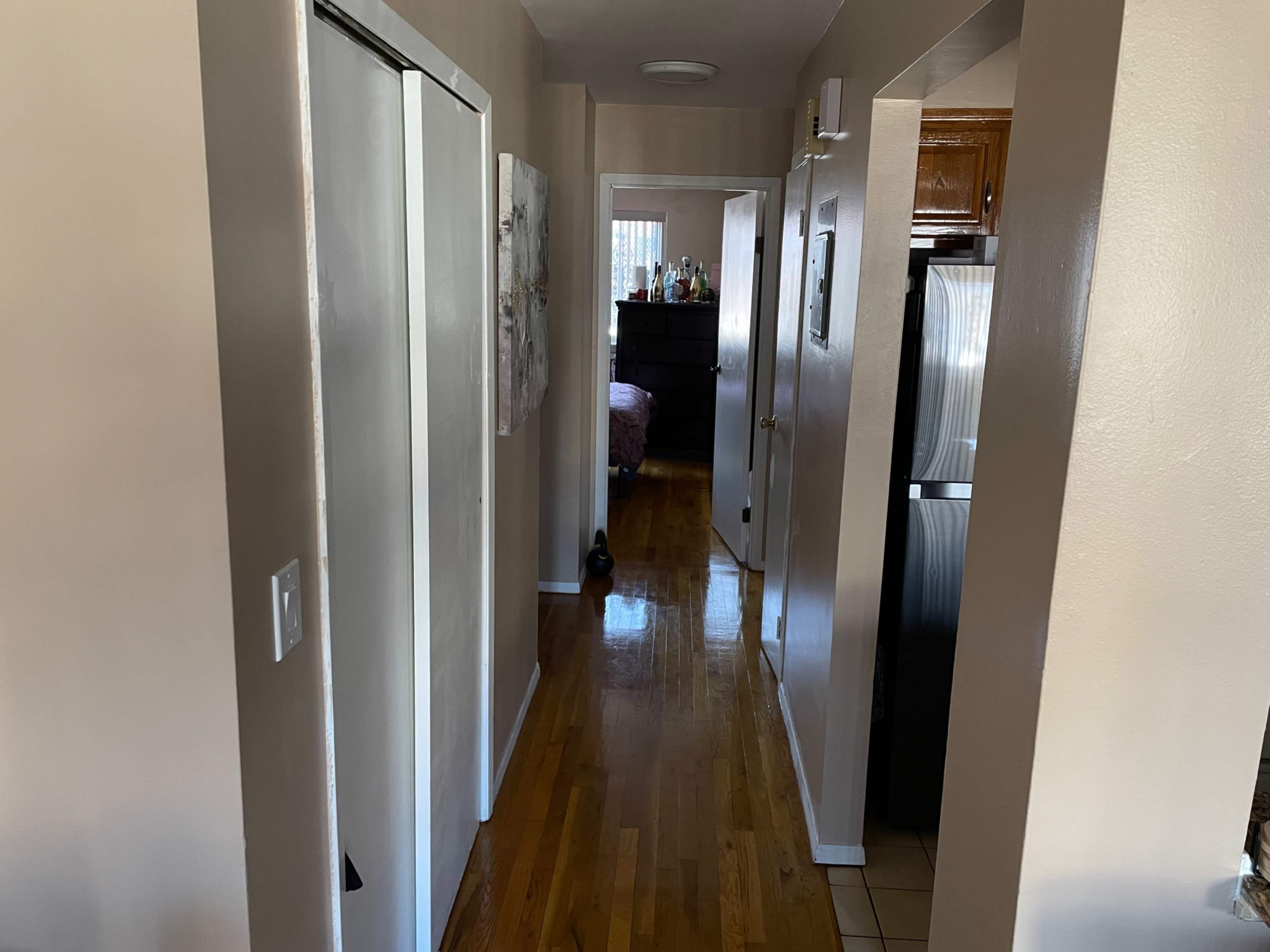 A narrow hallway with hardwood flooring, leading to a room in the background and featuring doors on either side.