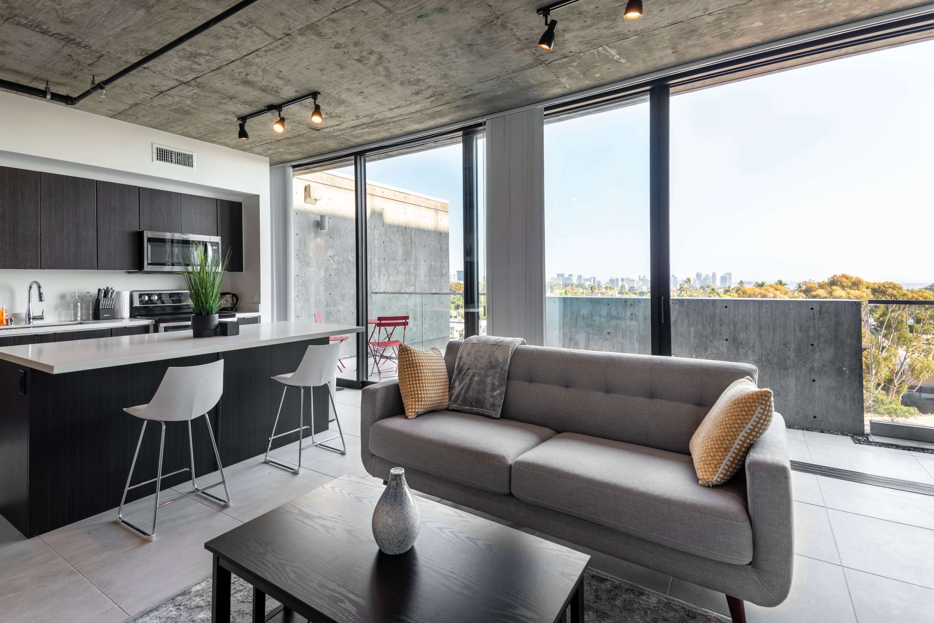 A modern apartment features a kitchen and living area with a view of the city skyline through large windows.