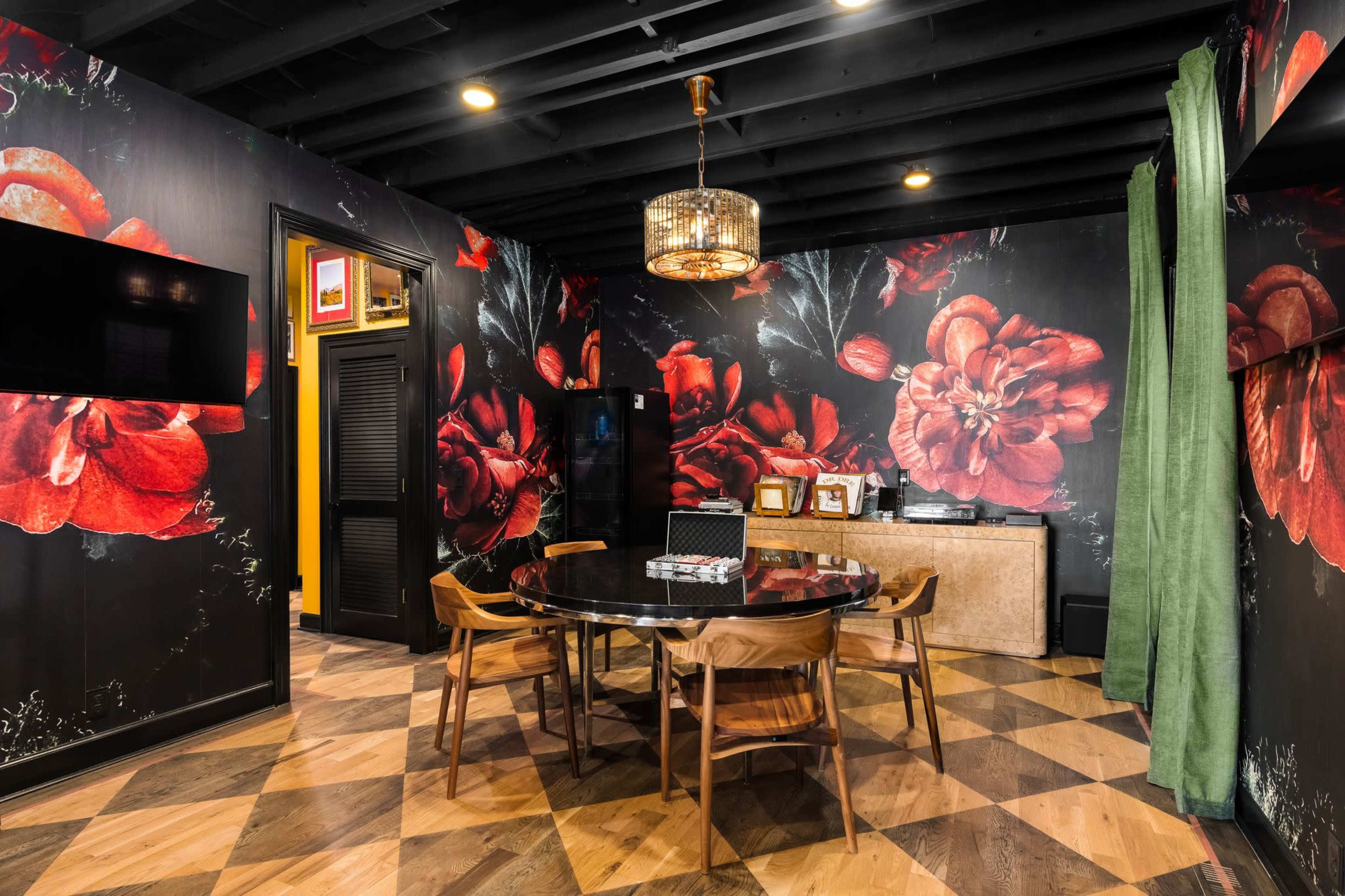 The image shows a dining area with a round table surrounded by wooden chairs, set against floral-patterned wallpaper and dark ceiling boards.