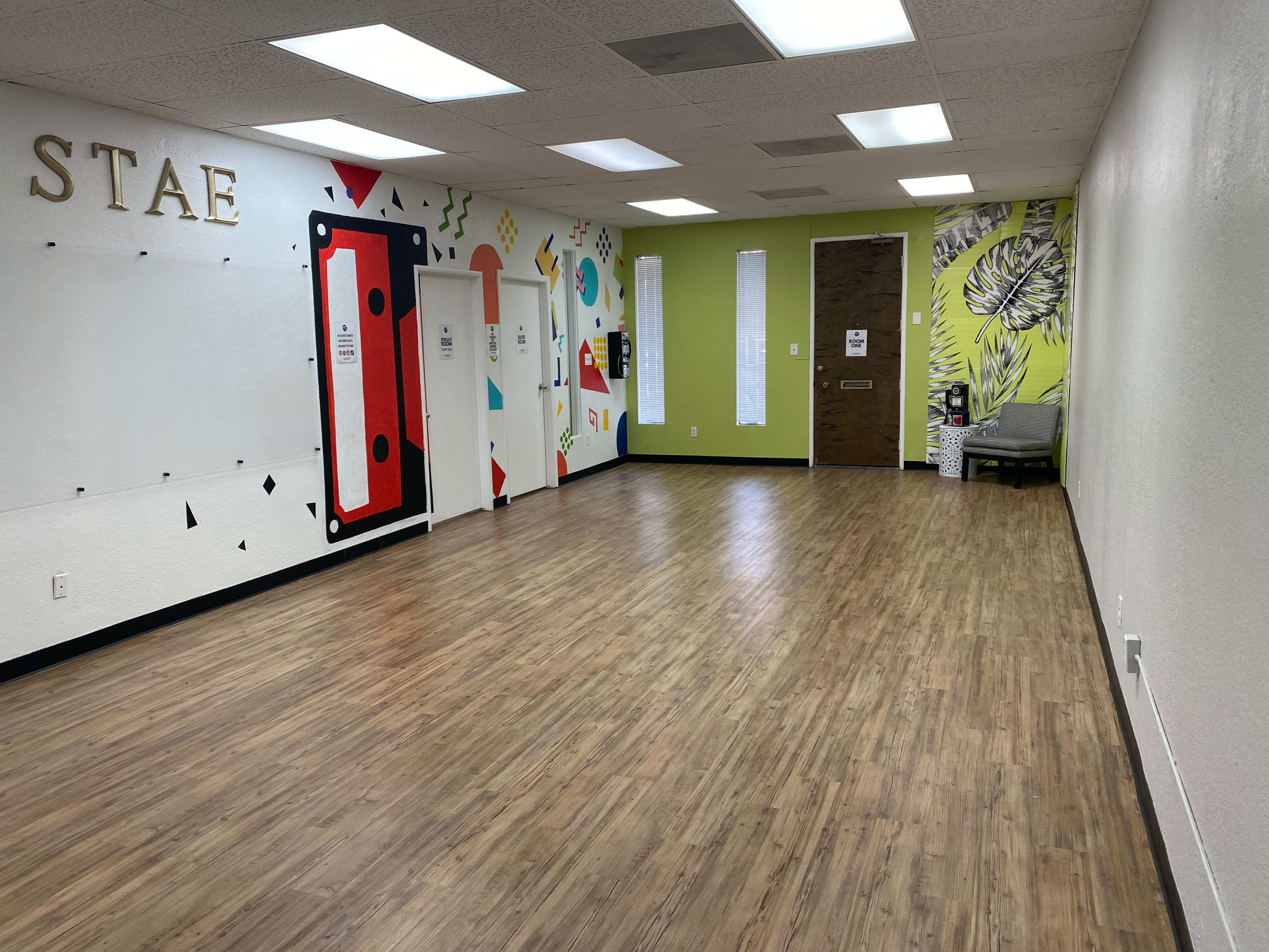 The image shows a spacious, brightly lit room with colorful wall art and a seating area in one corner.