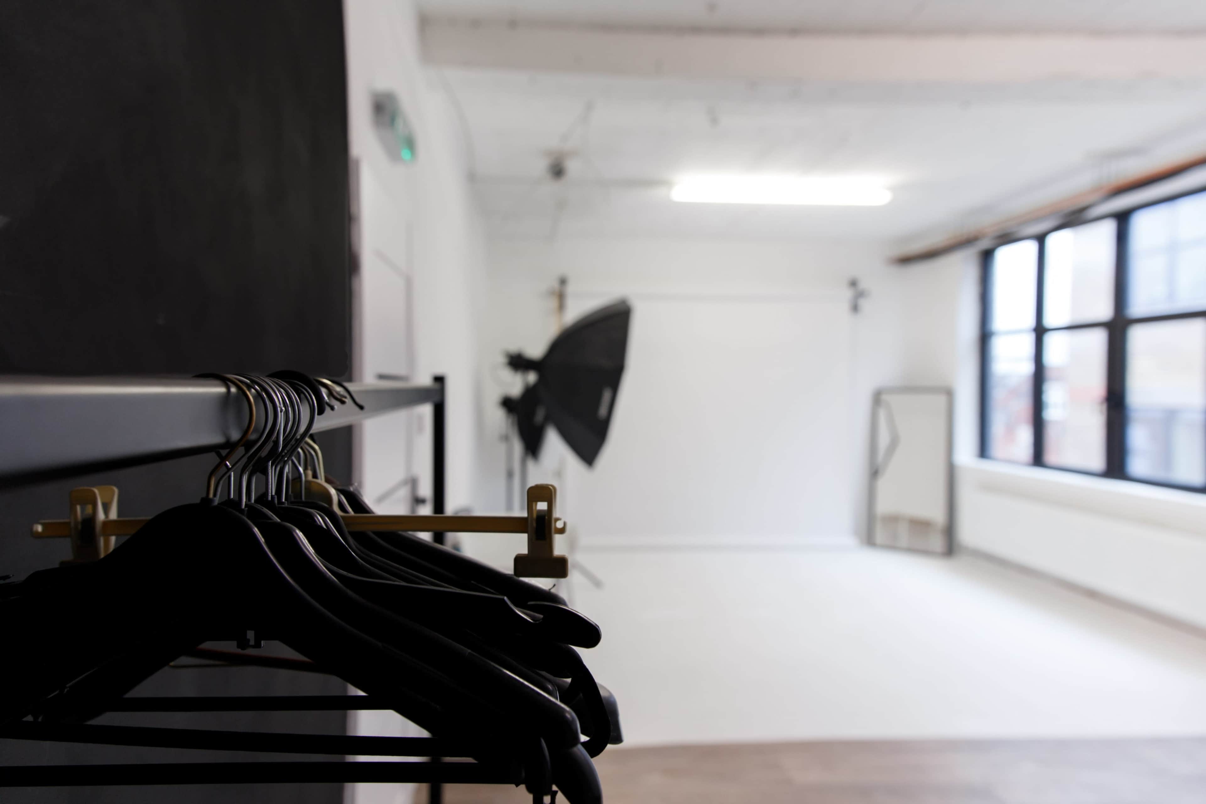 A minimalist photography studio with black clothing hangers in the foreground and lighting equipment positioned in the background.