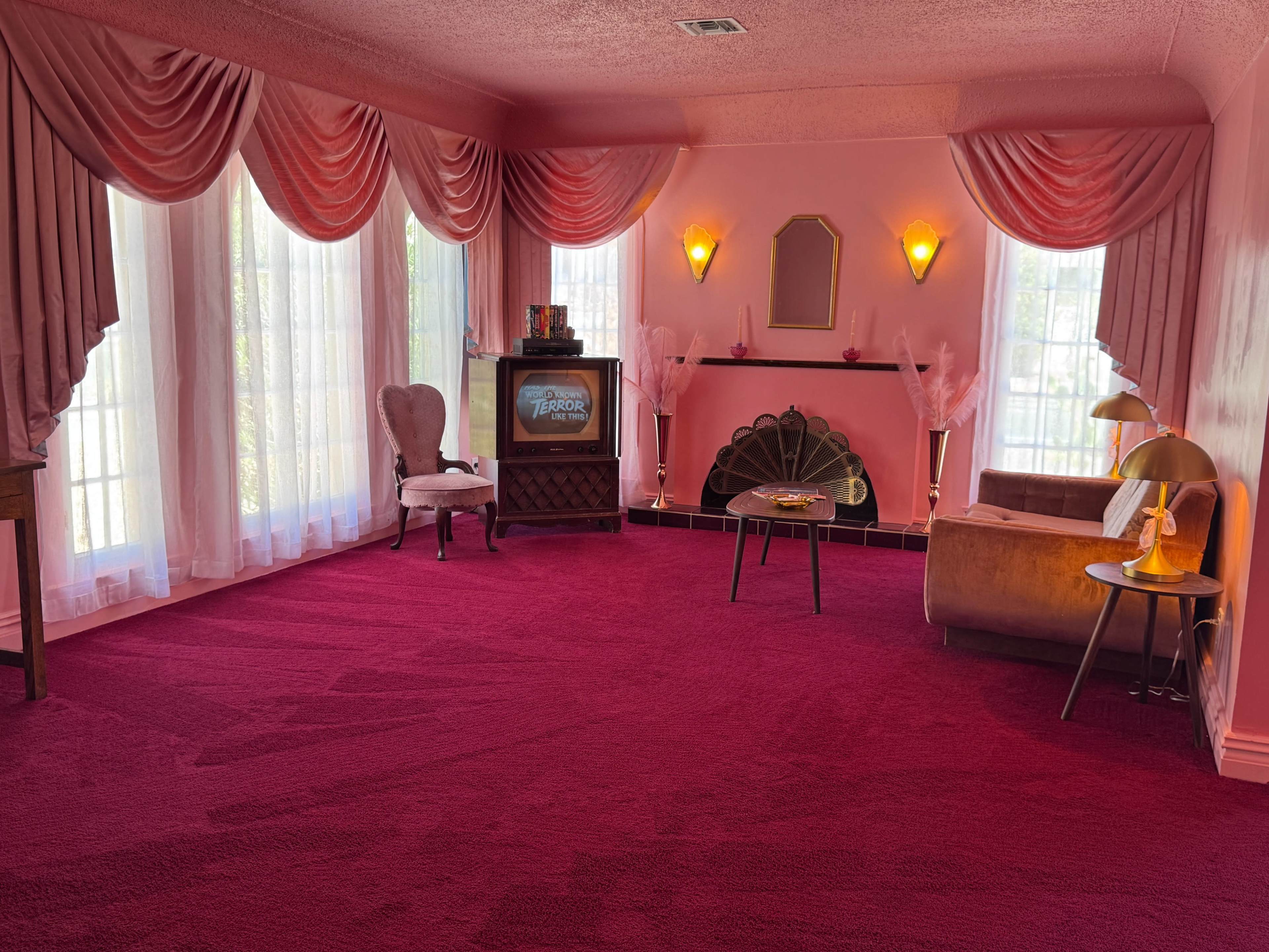 The scene features a retro living room decorated in shades of pink, with plush carpet, draped curtains, and vintage furniture including a television set and stylish lamps.