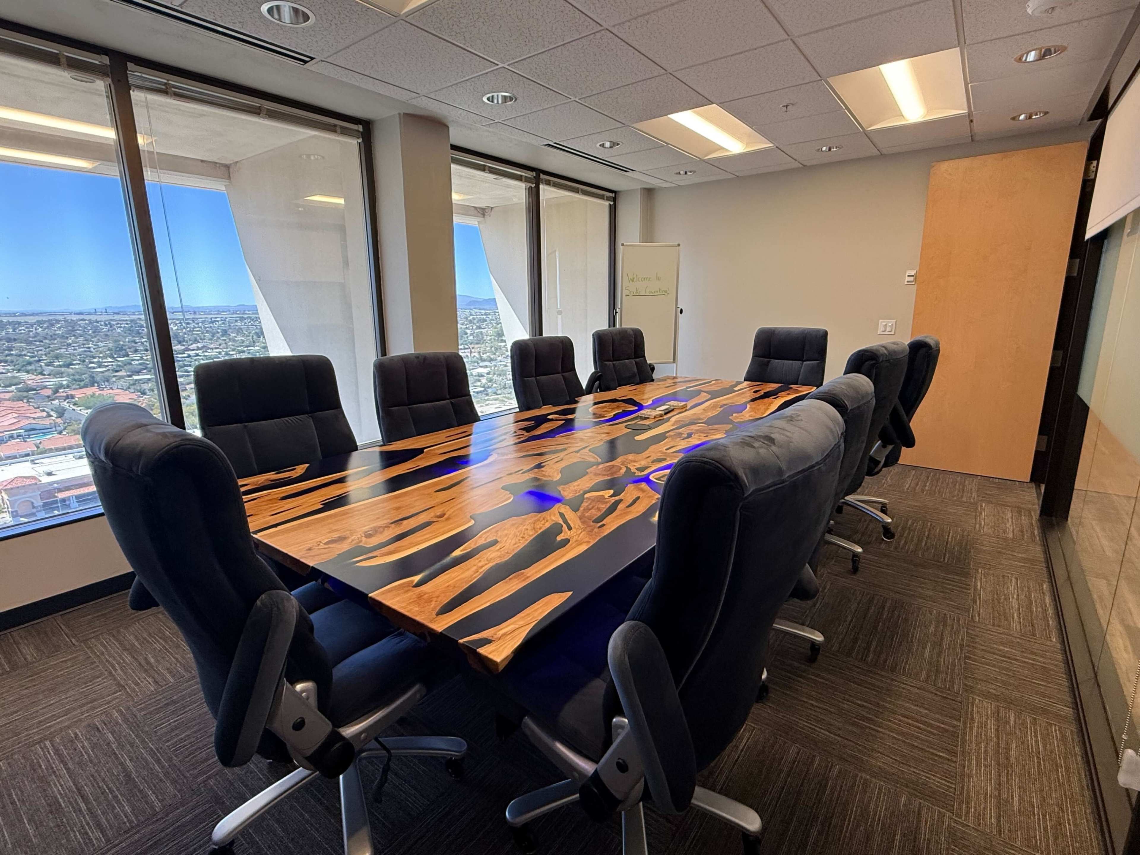 A large conference room features a polished wooden table surrounded by ergonomic chairs, with a view of the city skyline through the windows.