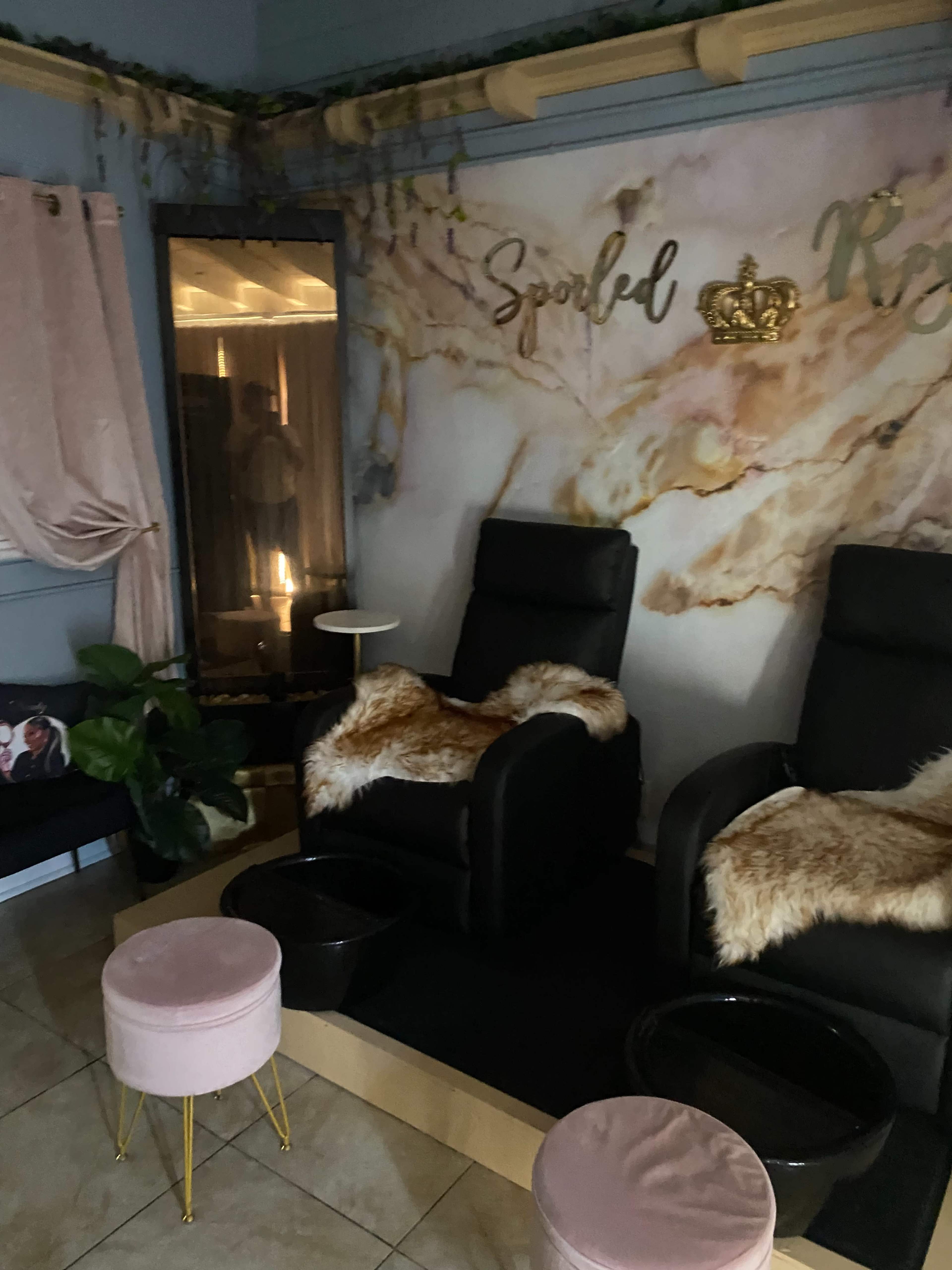 A cozy spa area featuring two black reclining chairs with fur throws, surrounded by decorative elements including a marble-patterned wall and soft pink accessories.