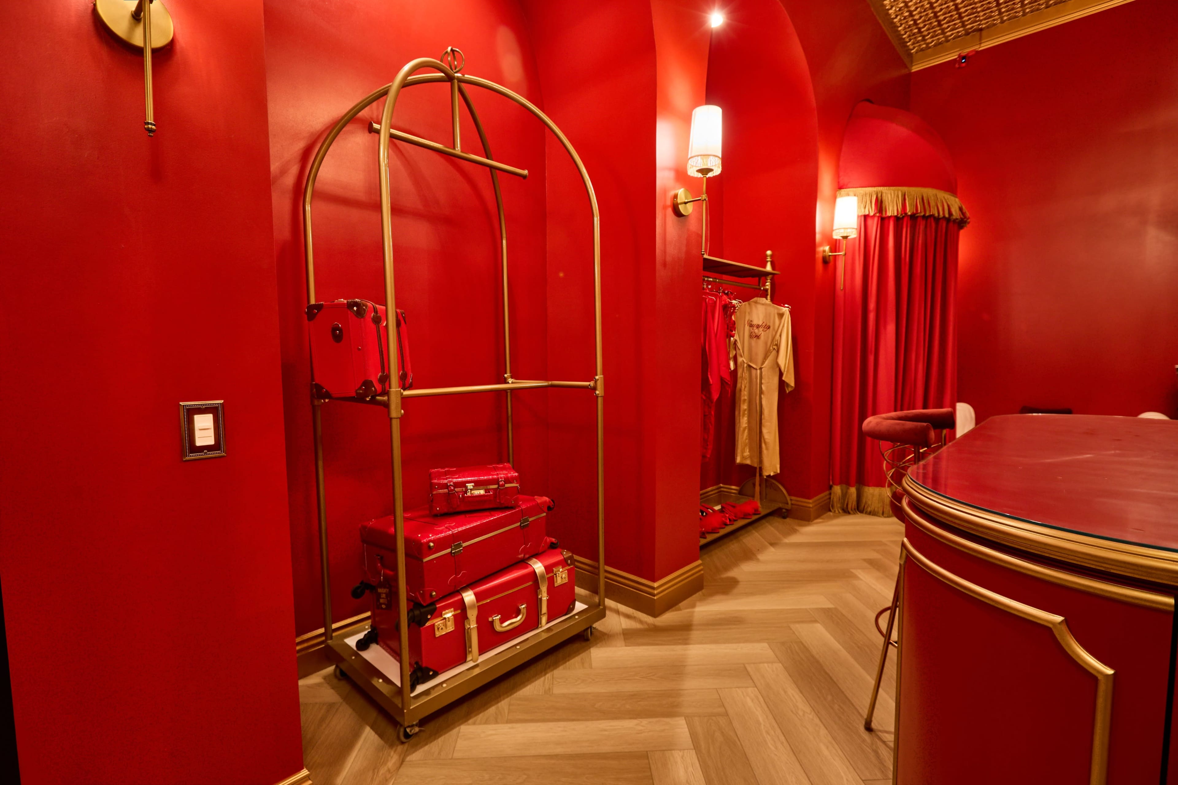 The image shows a boutique interior with red walls, a gold garment rack, and matching luggage stacked on a polished wooden floor.