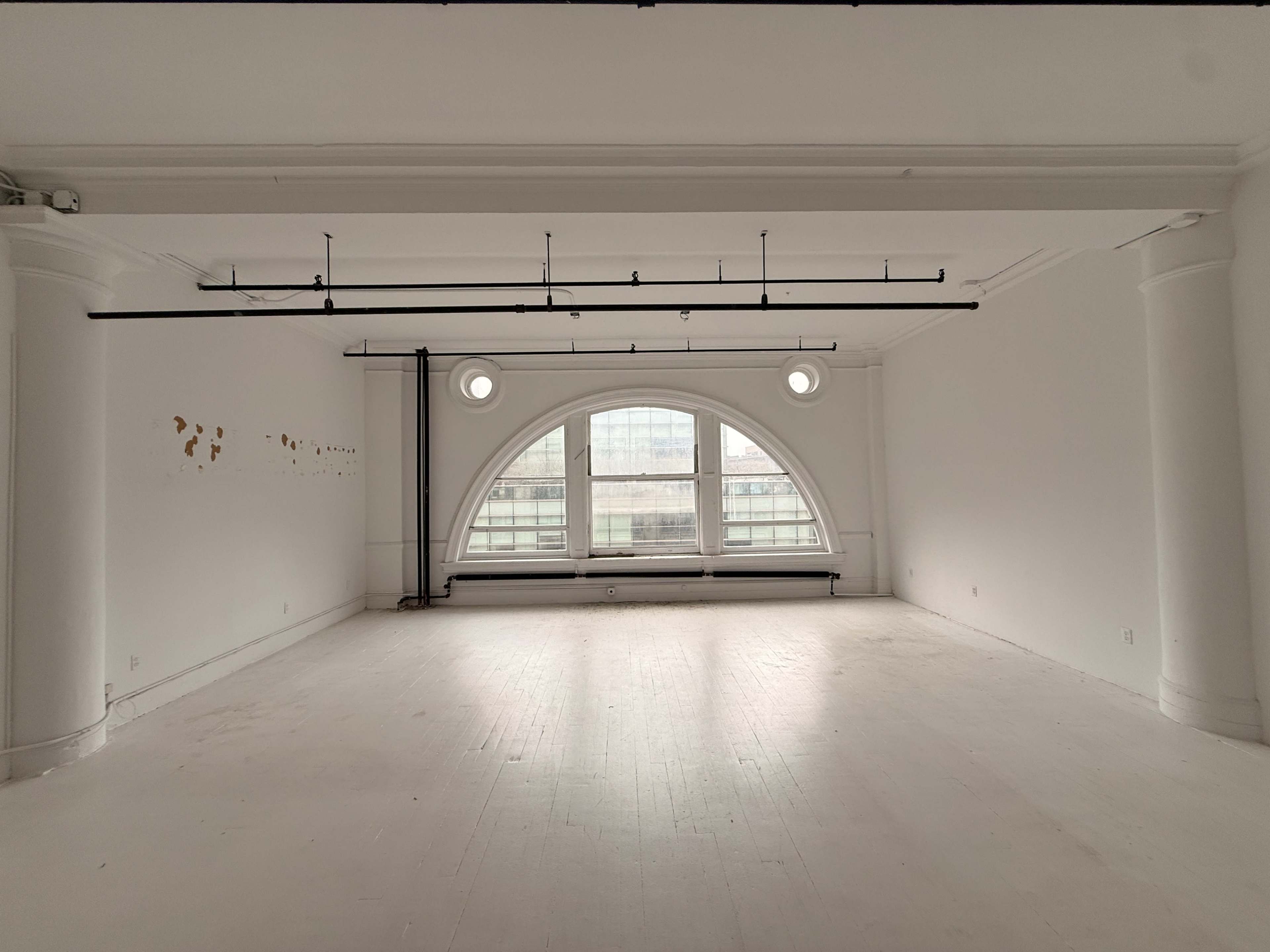 The image shows a spacious, empty room with large arched windows and a white floor.