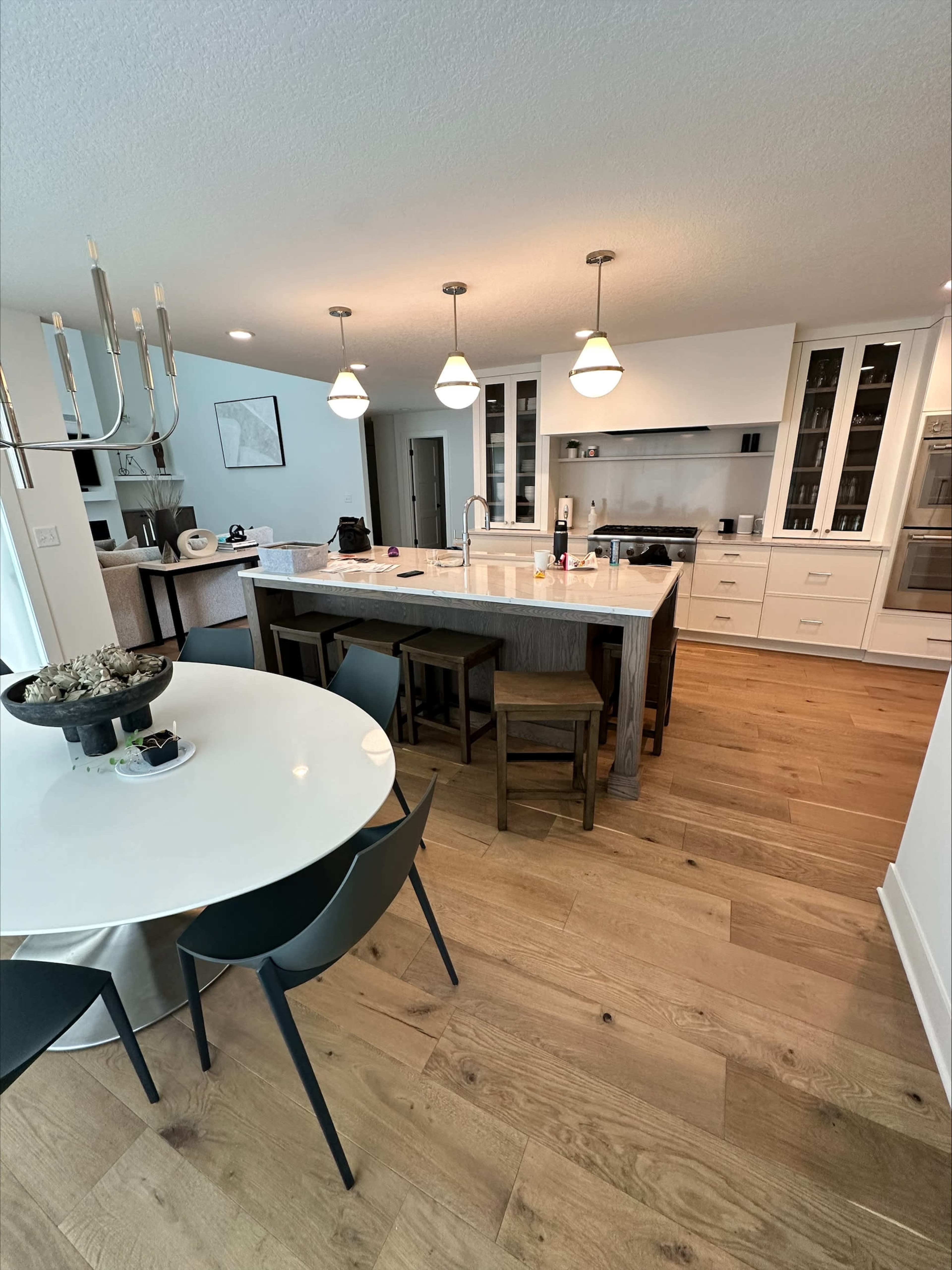 A modern kitchen features bright lighting, a large island with seating, and an adjacent dining area with a circular table.