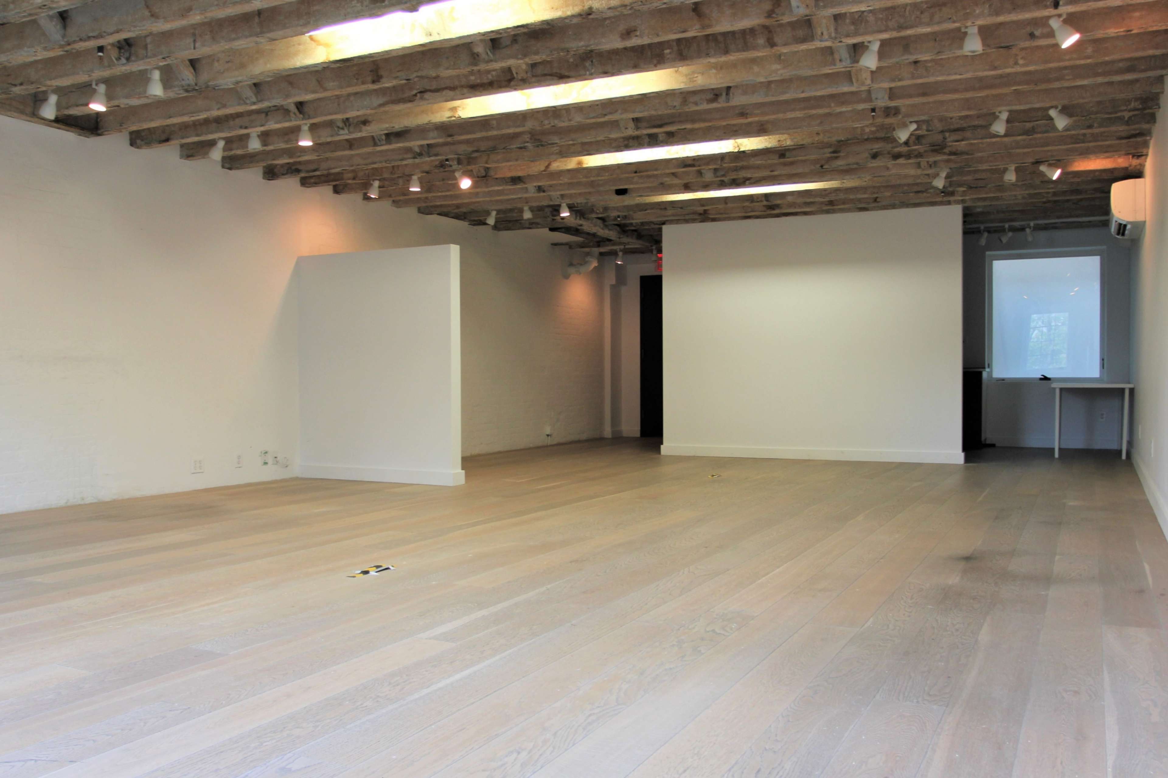 An empty room with wooden floors and exposed ceiling beams, featuring white walls and minimal furnishings.