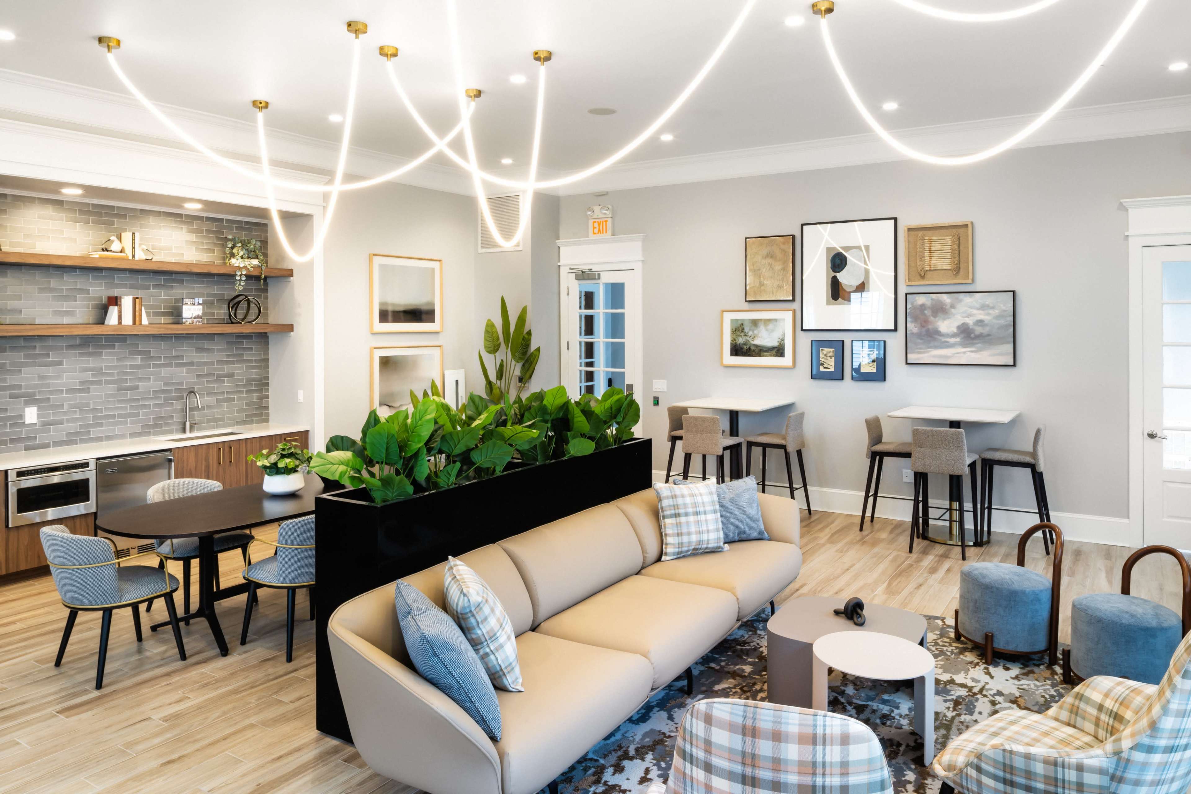 The image shows a modern lounge area with a sofa, dining table, kitchenette, and various decorative elements, illuminated by unique overhead lighting.