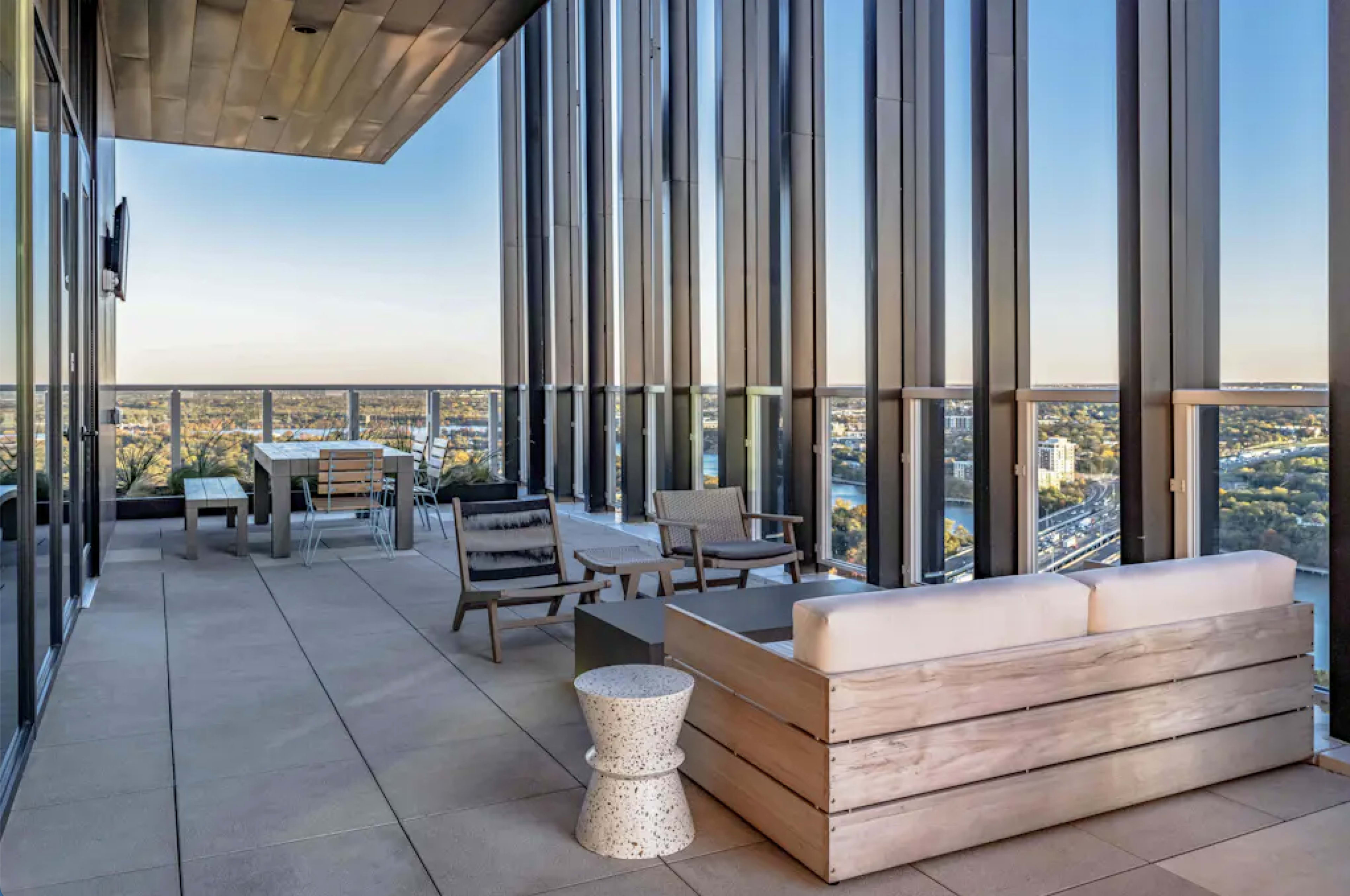 A modern balcony features sleek furniture and expansive glass walls, offering a panoramic view of the city skyline.